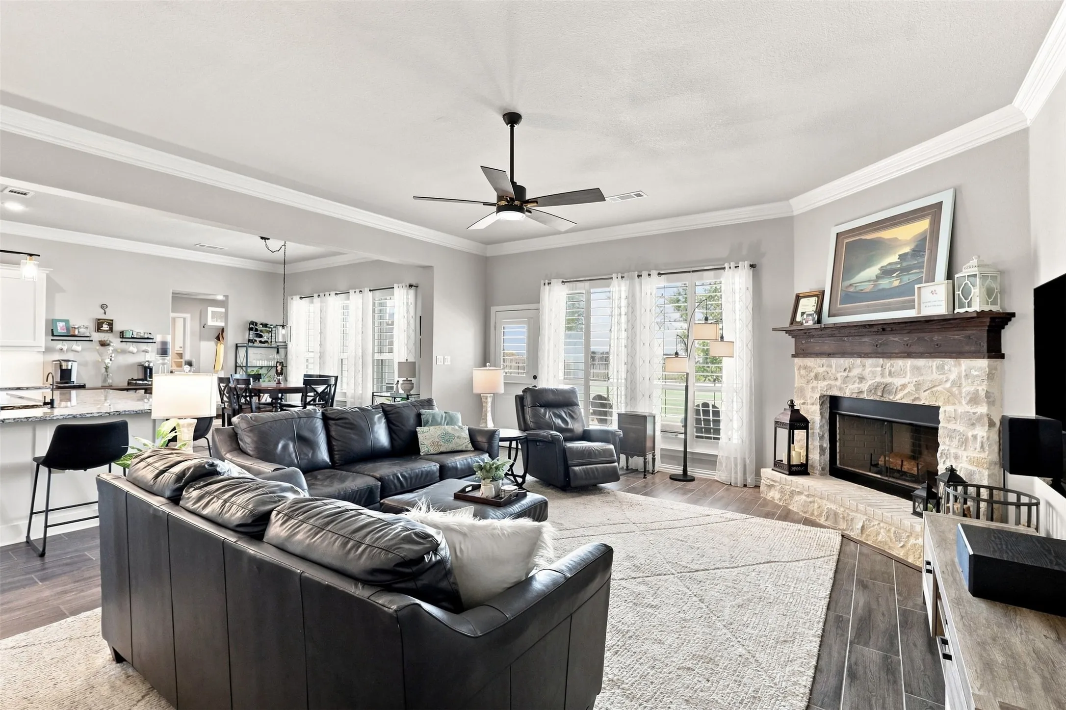 Stone-clad fireplace with a wood mantel, crown molding, and wood-finish flooring