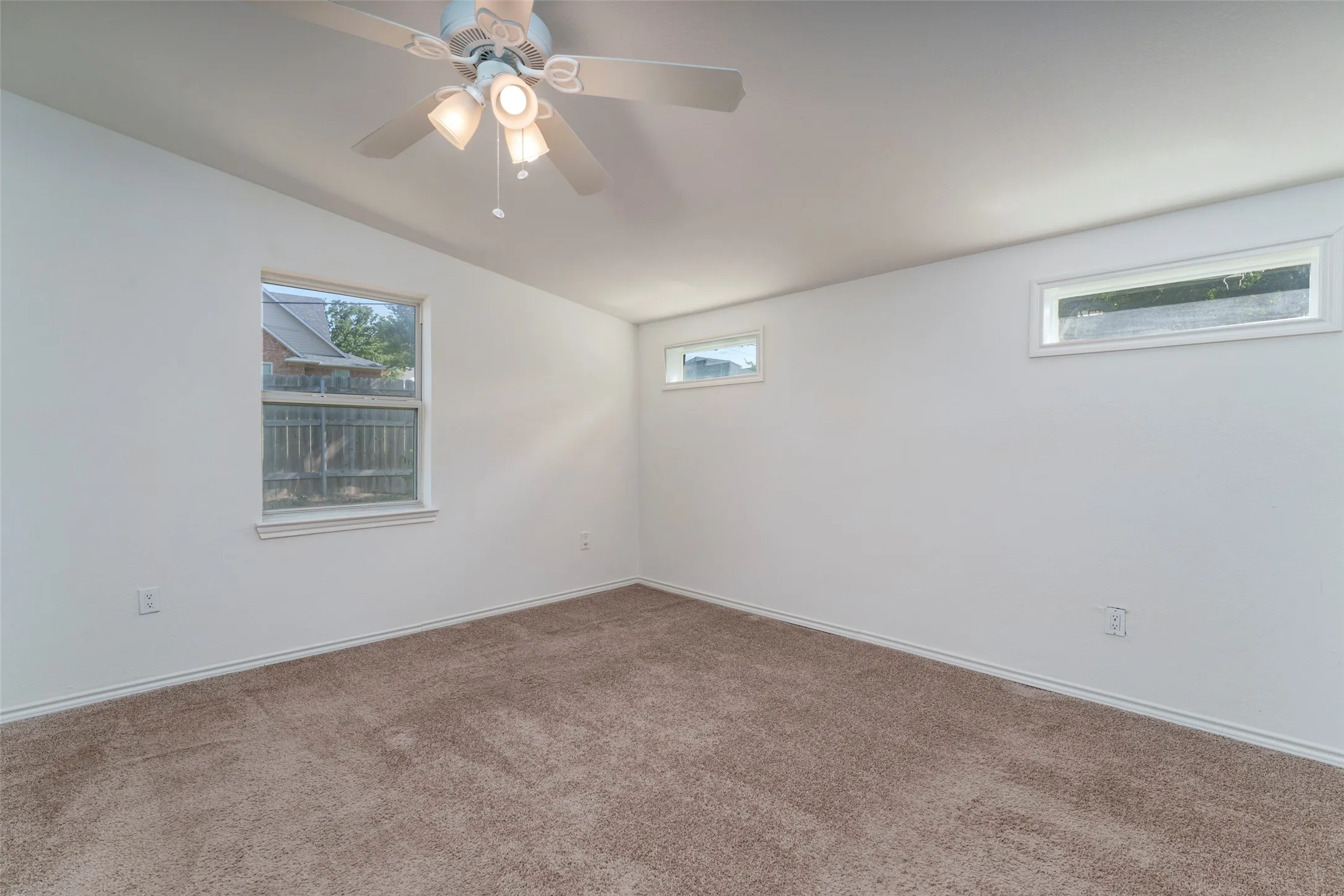 Carpeted flooring, white walls, multiple windows, and a ceiling fan with integrated lighting