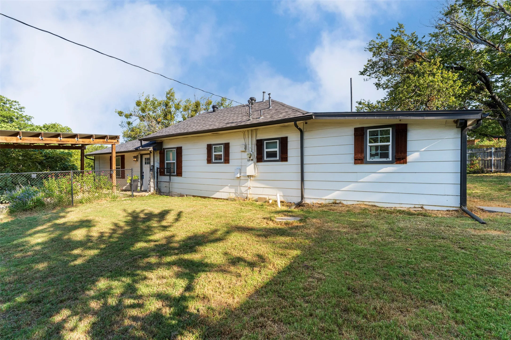 White siding exterior with dark brown window shutters, dark gray roof, and dark rain gutters