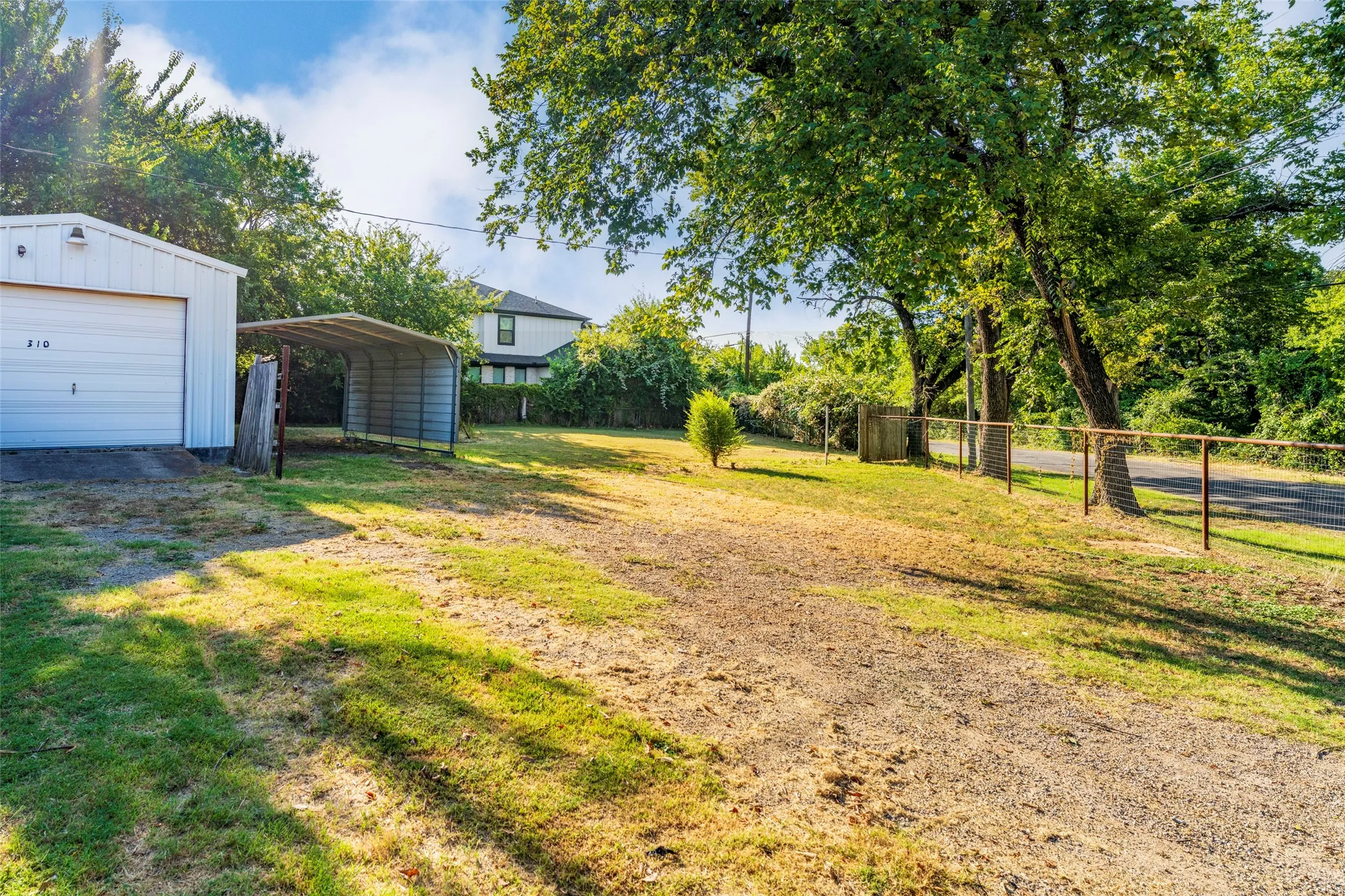 Detached garage with a roll-up door, an open-sided carport, and a gravel driveway