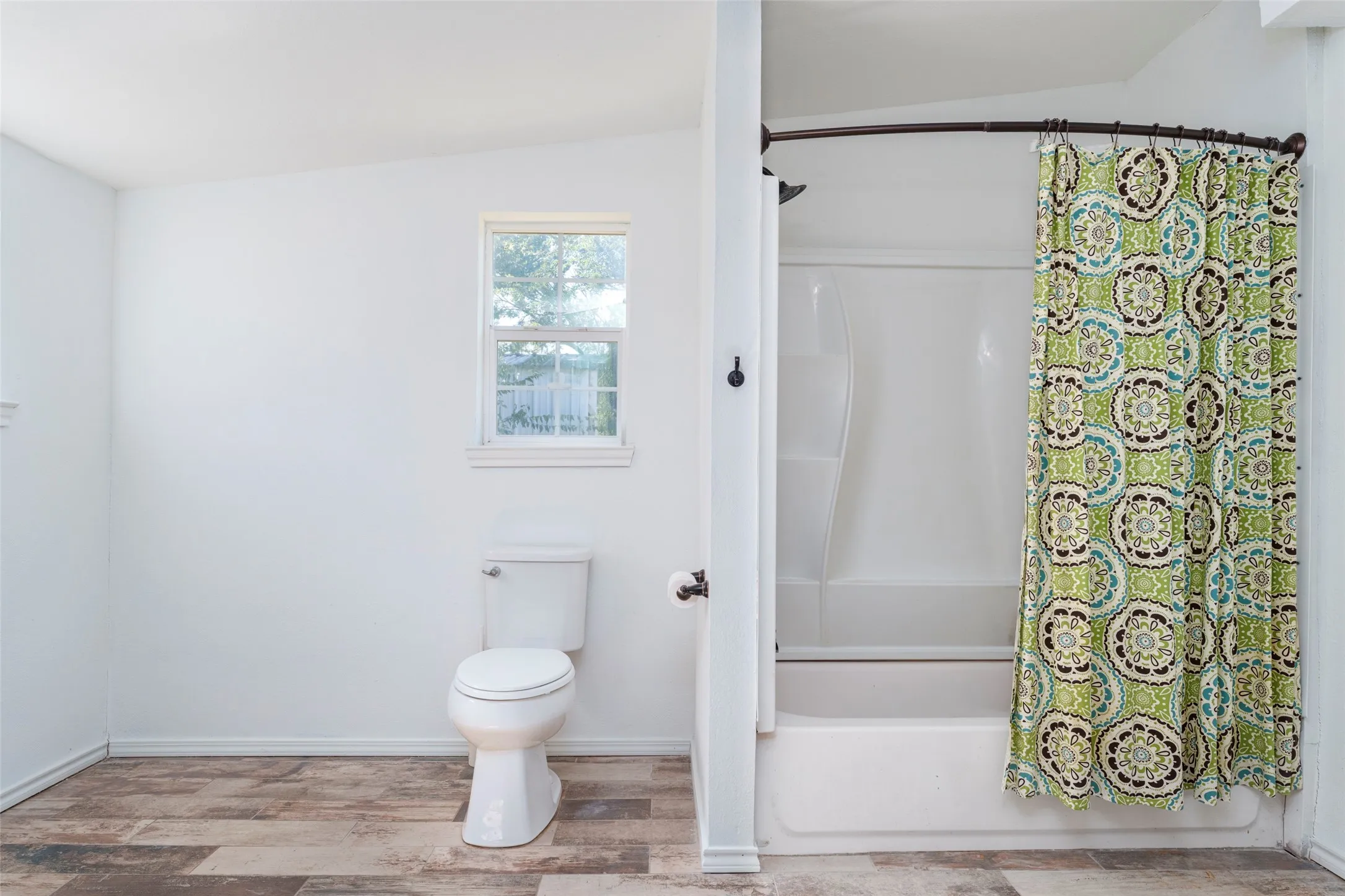 Windowed bathroom featuring a toilet, a full bathtub, and wood-finish flooring