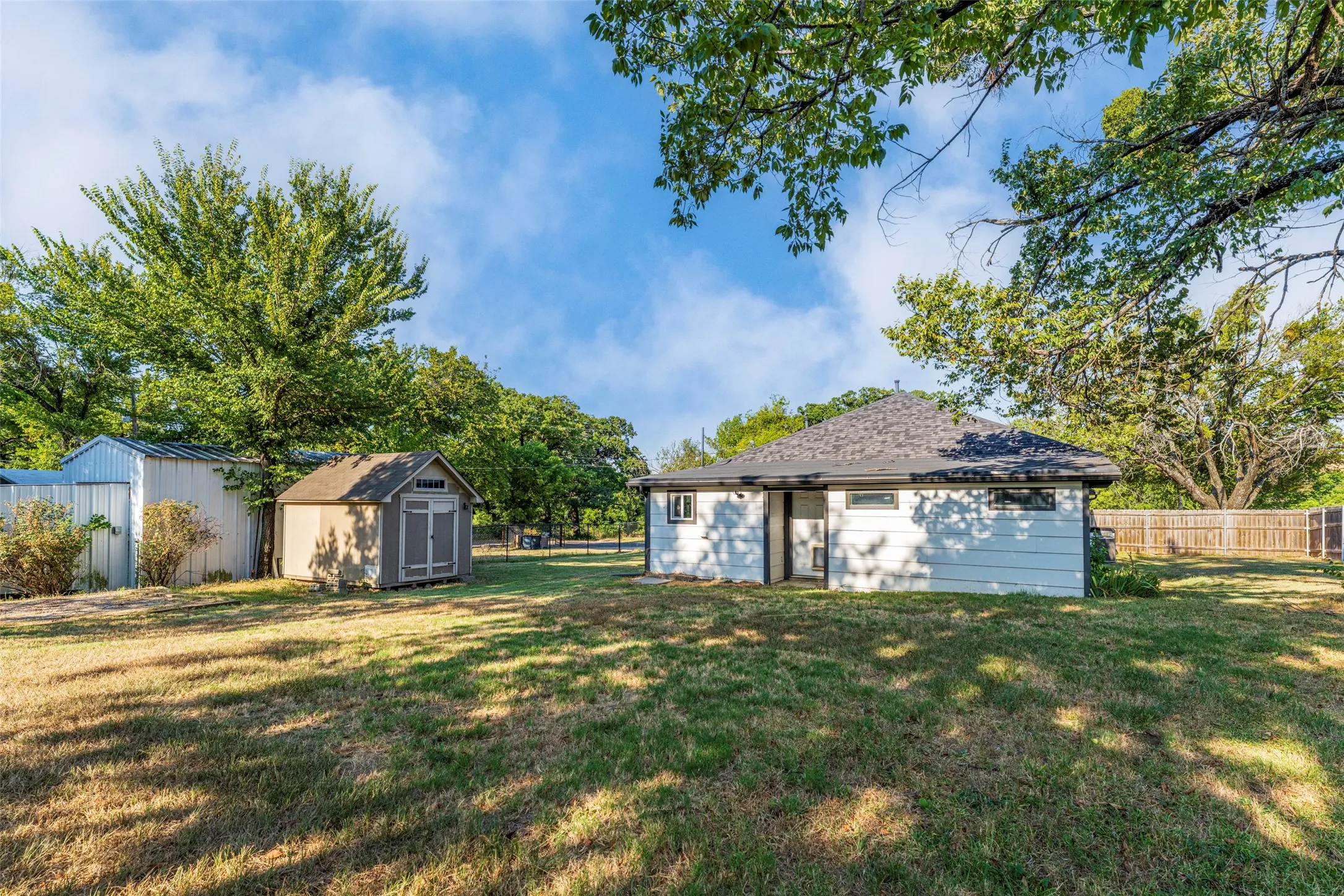 Expansive rear yard featuring a detached storage shed, a metal storage building, and a wood privacy fence