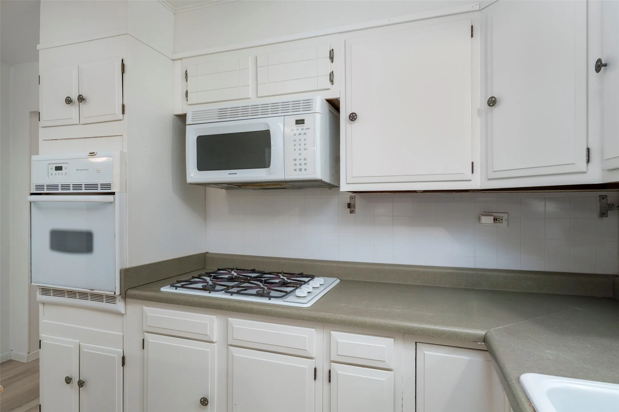 White cabinetry with circular hardware, built-in wall oven, built-in microwave, gas cooktop, and neutral countertops