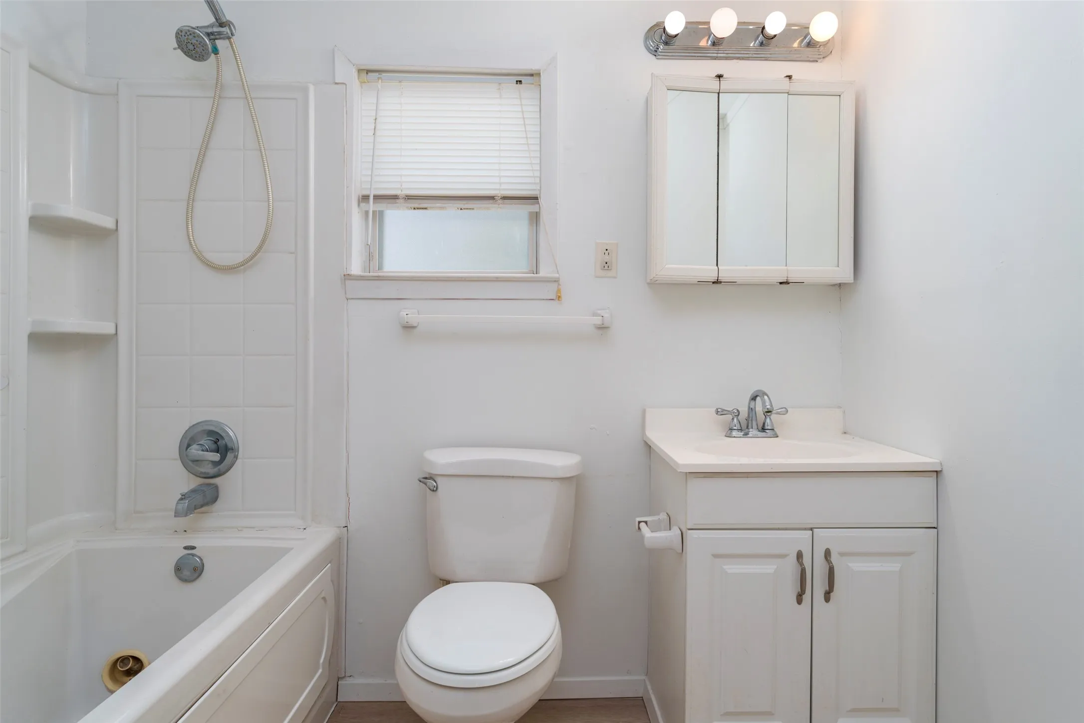 White tiled shower/tub combination with built-in shelving, white vanity with integrated sink, and medicine cabinet with mirror