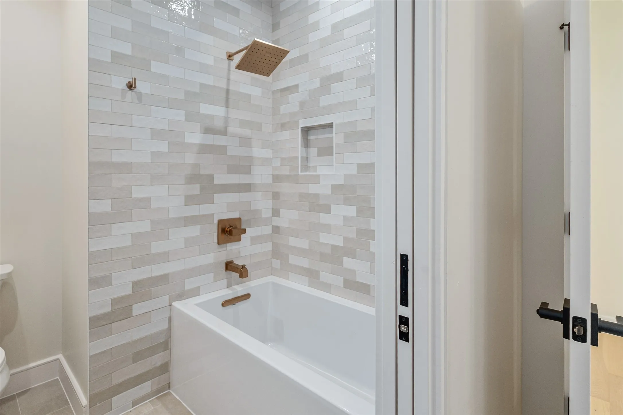 Bathtub and shower combination featuring a tiled surround, recessed shower niche, and bronze fixtures