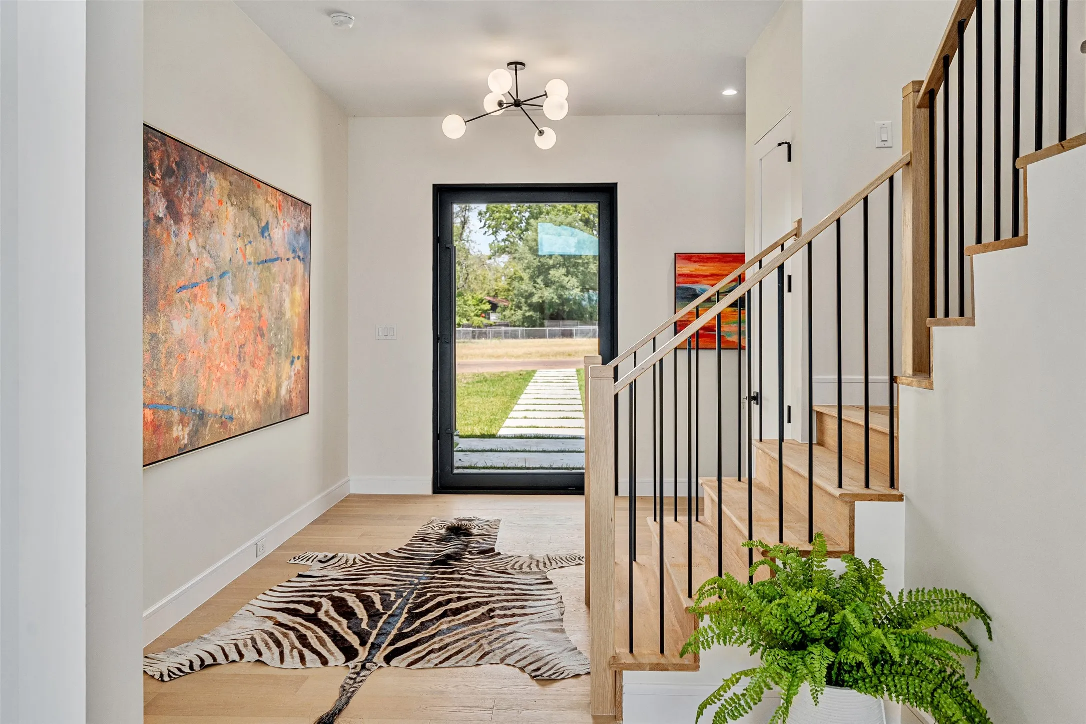 Entryway featuring light wood-finish flooring, a modern chandelier, and a staircase with a wood handrail and black balusters