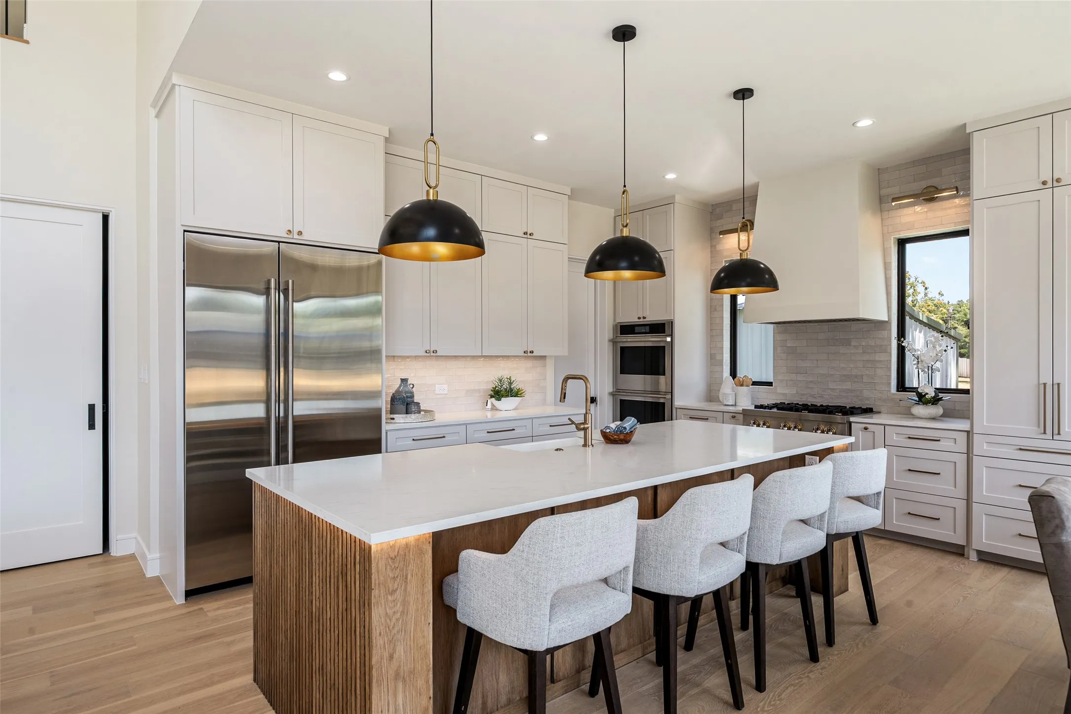 Gourmet kitchen with a large central island, light wood-finish flooring, integrated stainless steel refrigerator, white cabinetry, and a tile backsplash