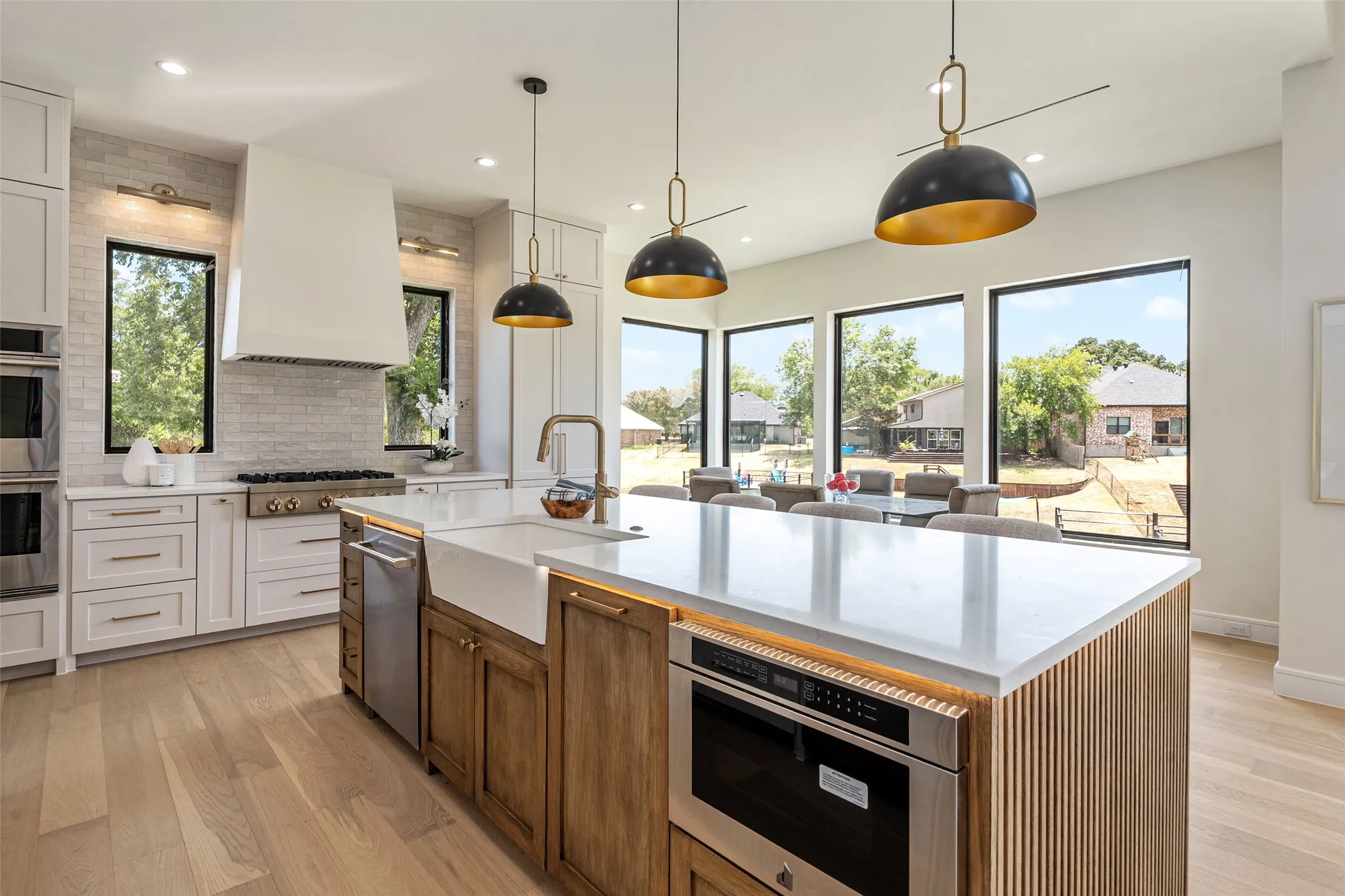 Kitchen featuring a large center island with a farmhouse sink, stainless steel appliances, light-toned wood-finish flooring, and multiple large windows
