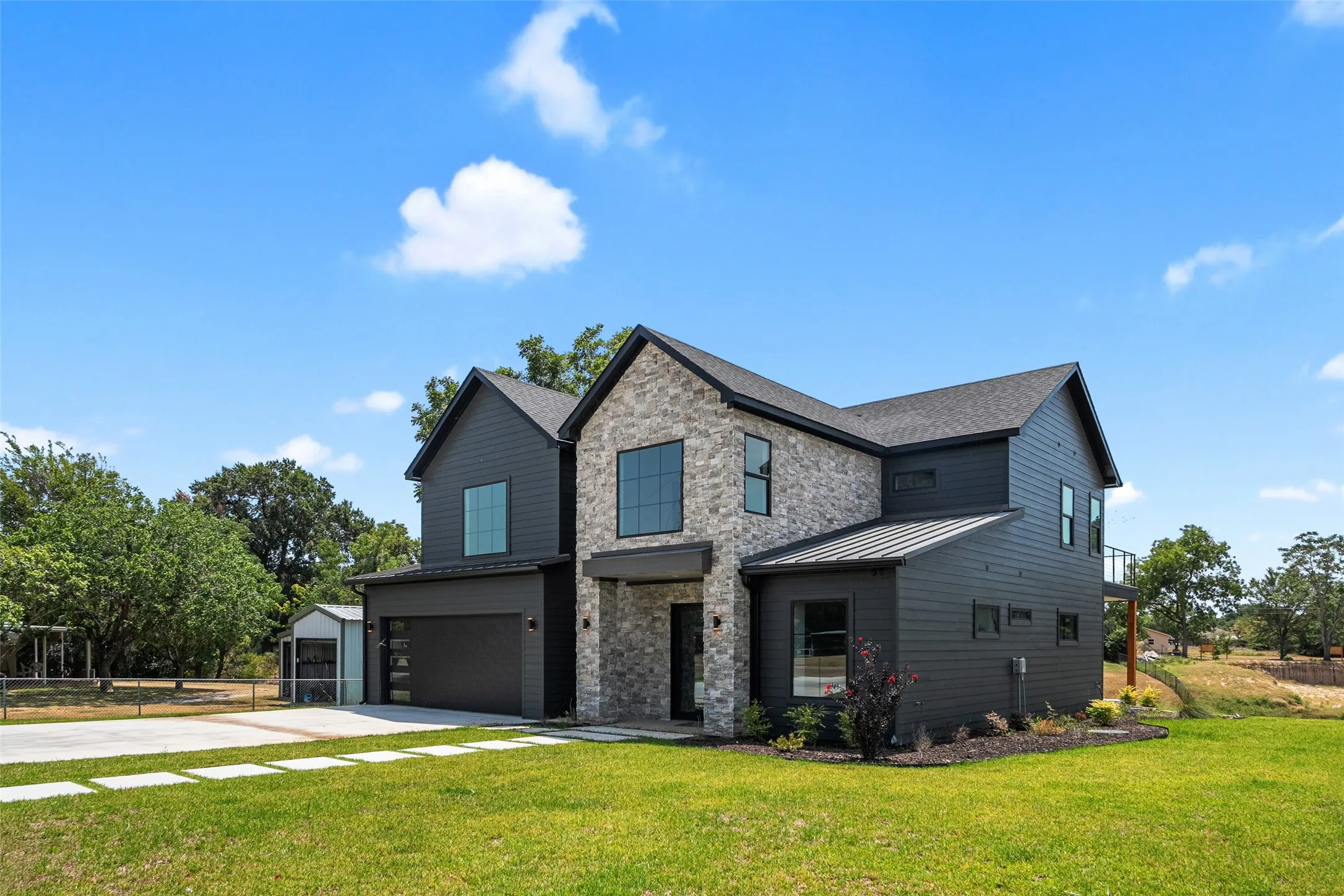 Contemporary architecture featuring a stone and dark siding exterior, multi-pane windows, a two-car garage, and a covered entry