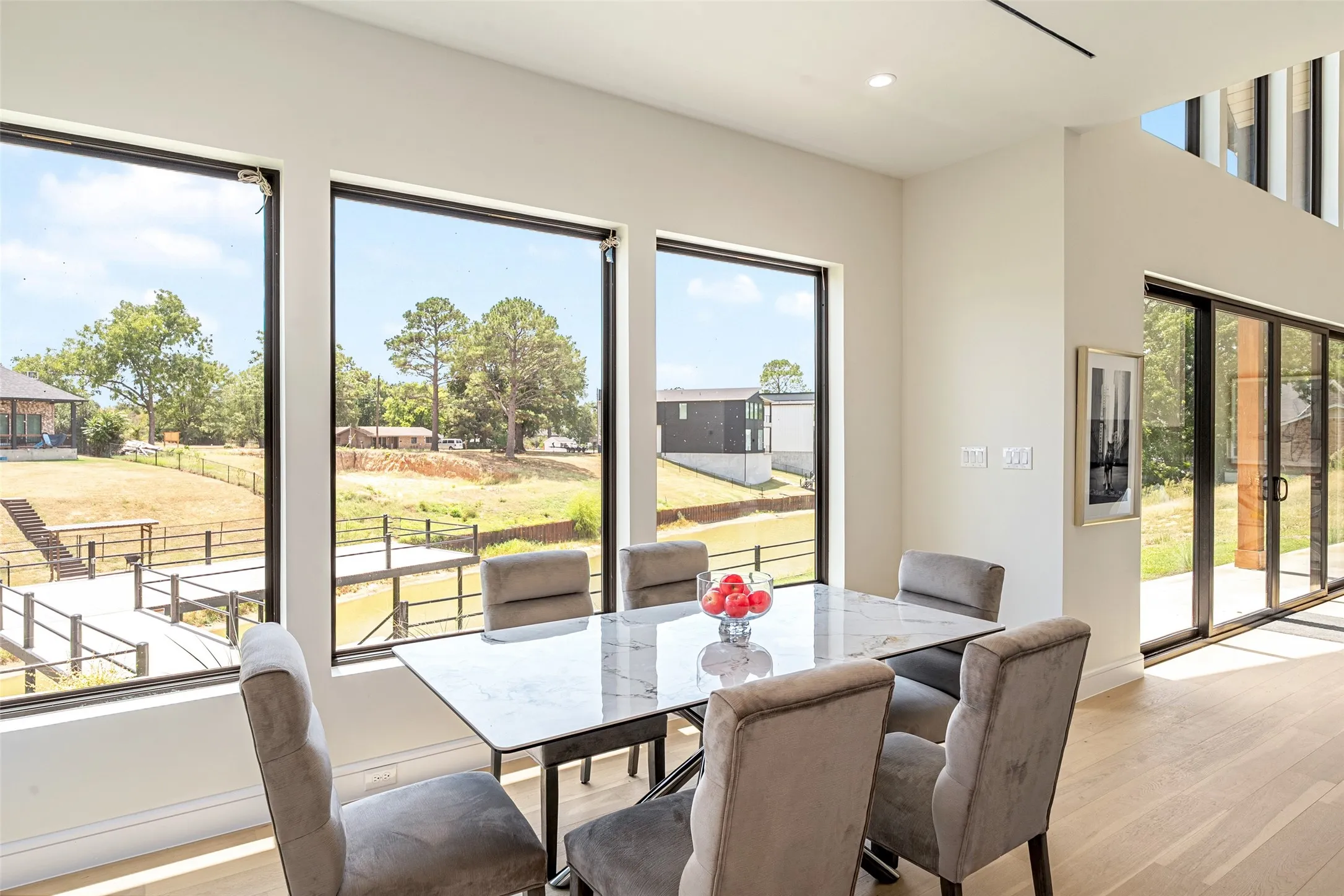 Expansive windows, light wood-finish flooring, high ceilings, and a sliding glass door