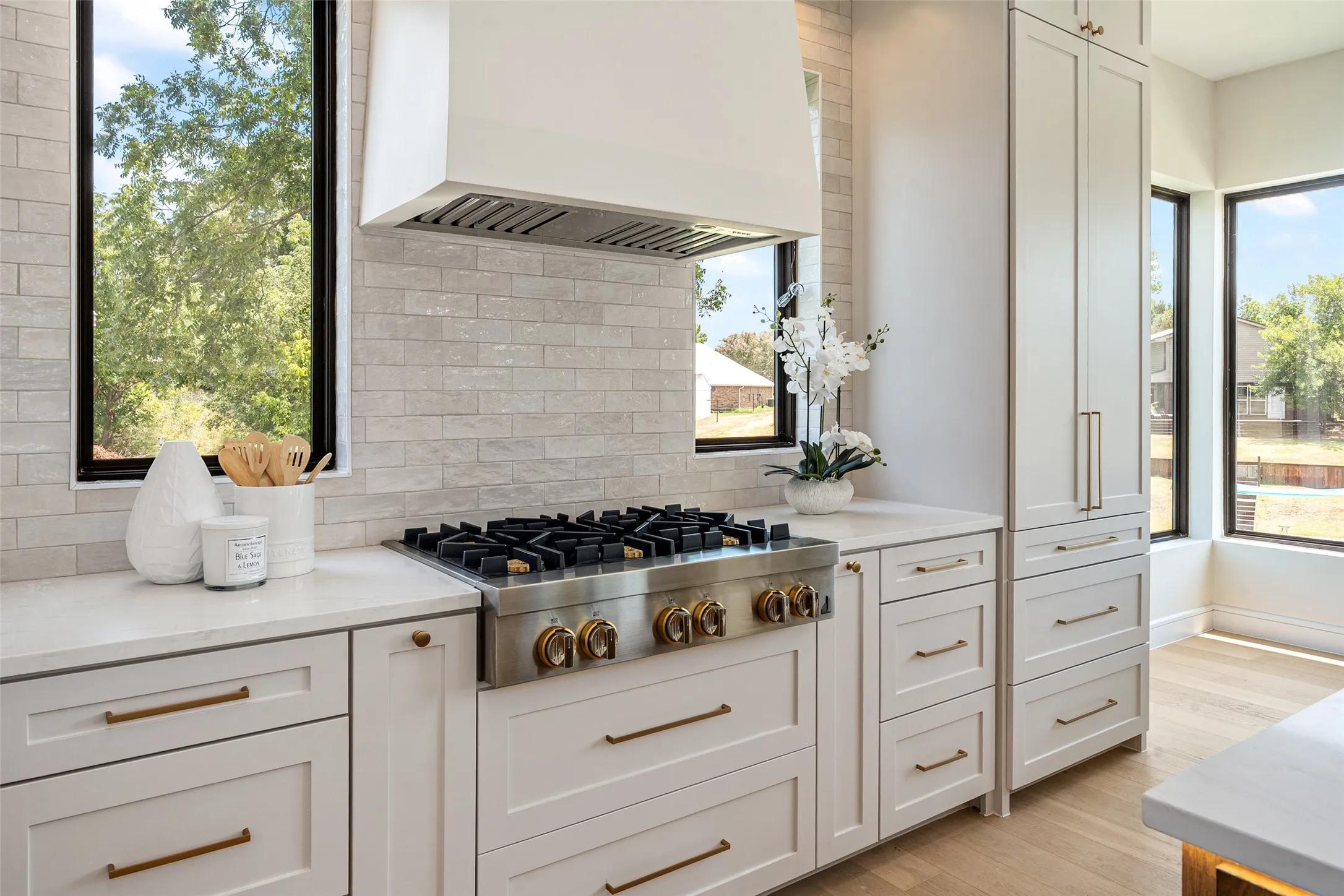 Gourmet kitchen featuring a professional-grade gas range, built-in refrigerator, white shaker cabinetry, light-toned stone countertops, and a subway tile backsplash