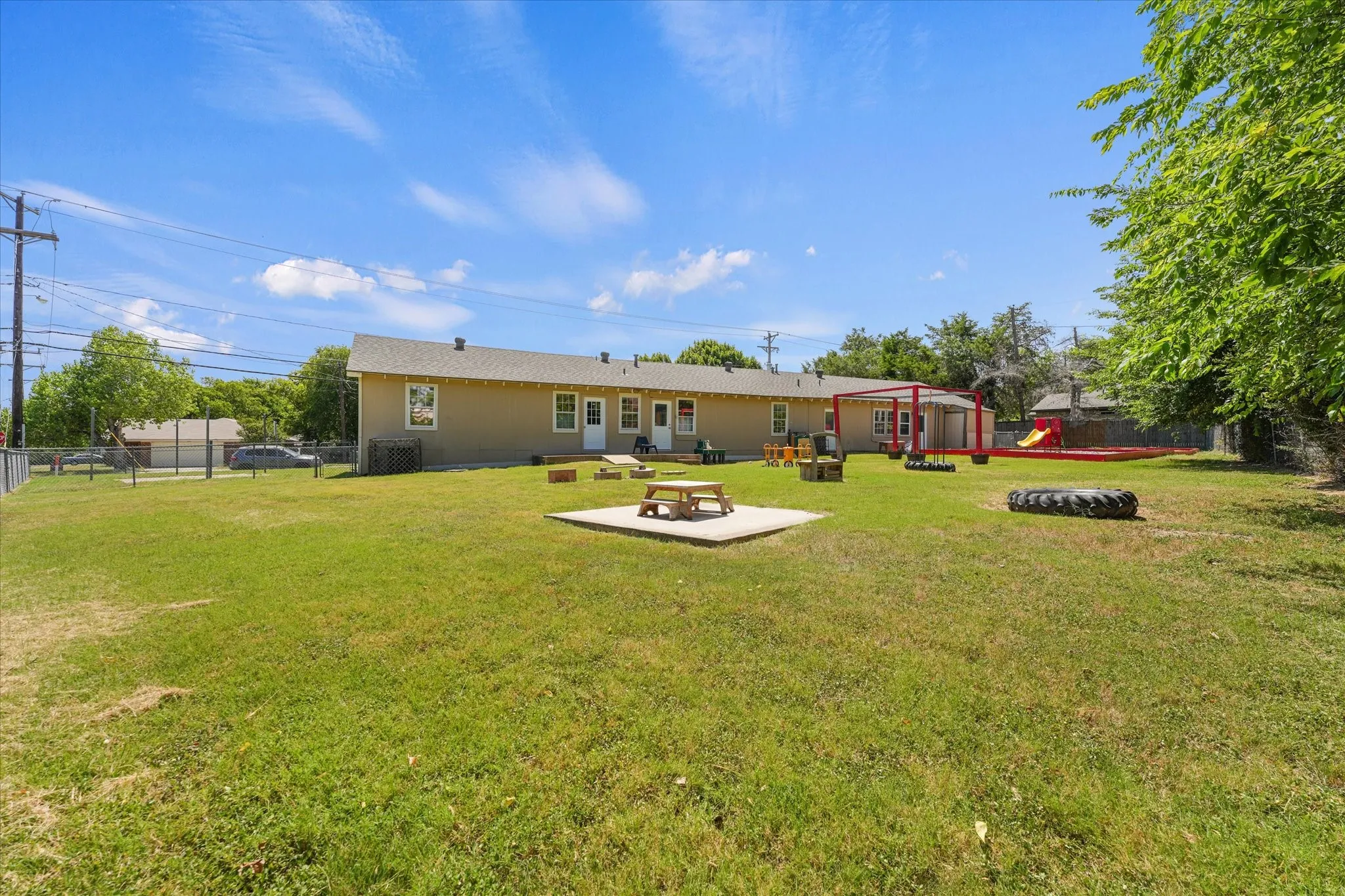 Expansive grassy yard featuring a concrete patio, a red-framed outdoor structure, and a perimeter fence