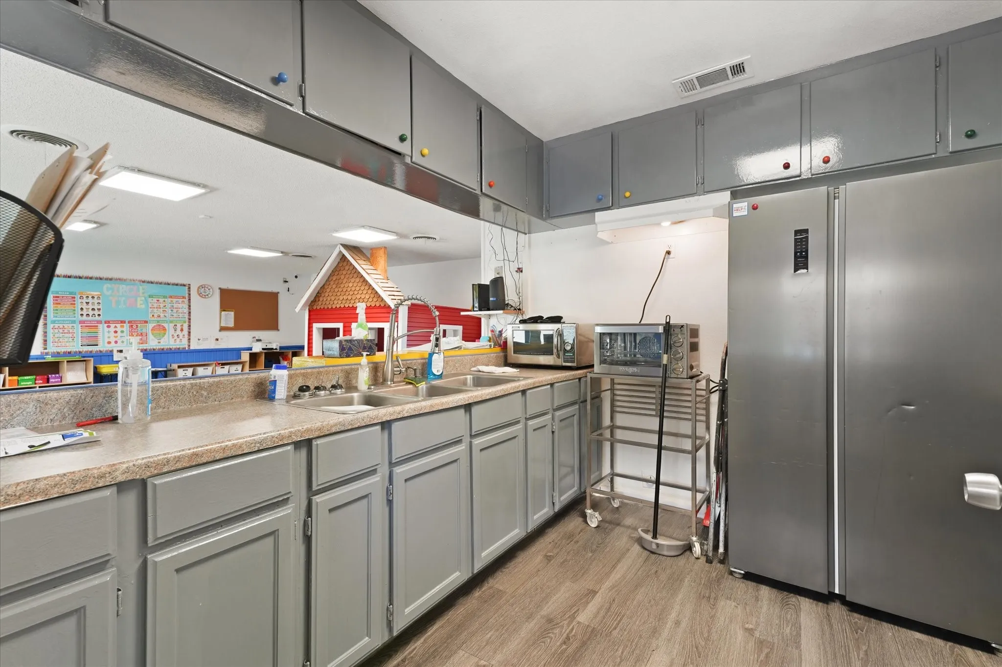Spacious kitchen featuring gray cabinetry with brushed nickel hardware, granite countertops, stainless steel appliances including a large refrigerator, and wood-finish flooring throughout