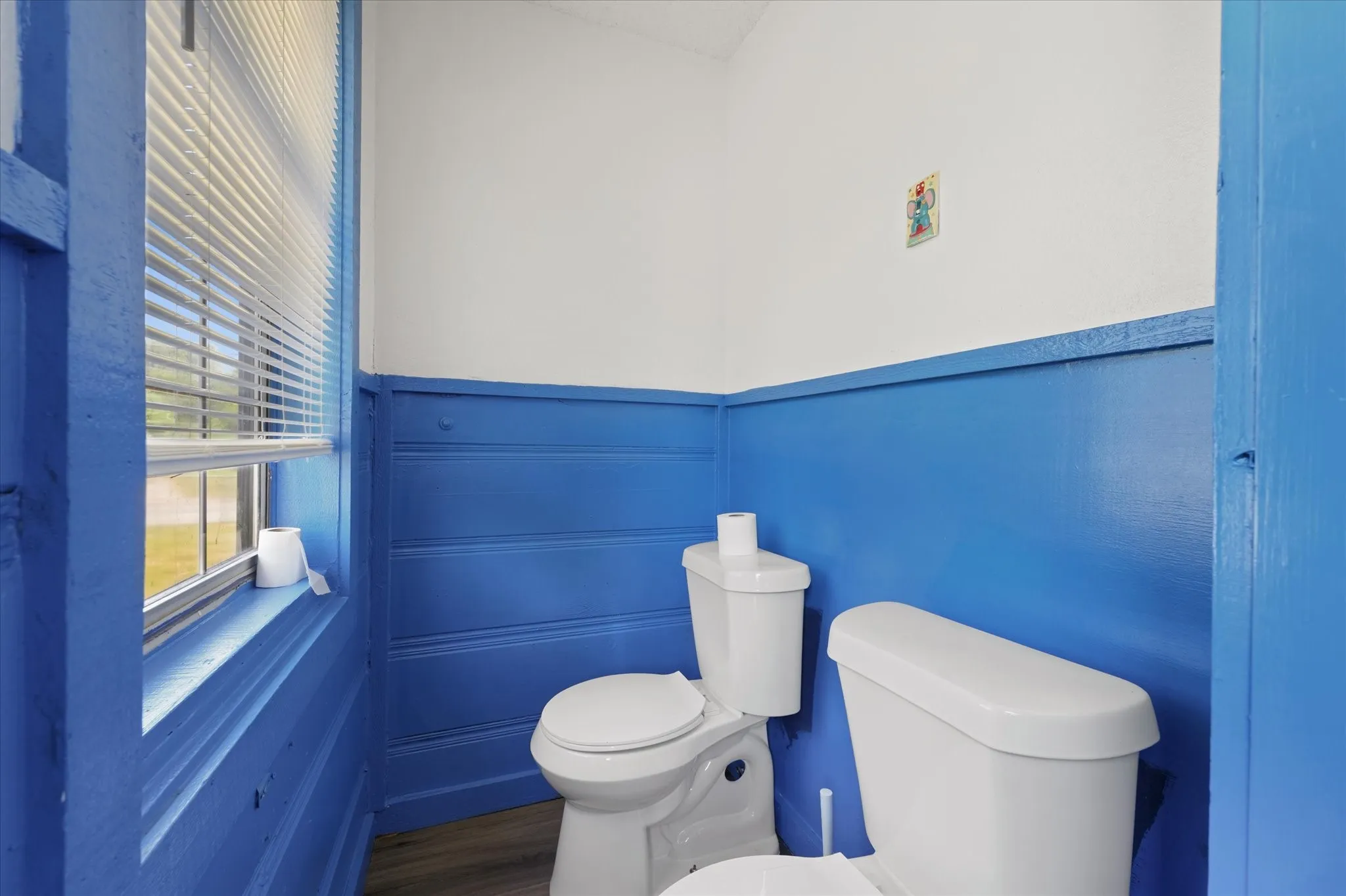 Bright powder room featuring vibrant blue wainscoting with horizontal shiplap detailing, white upper walls, and wood-finish flooring