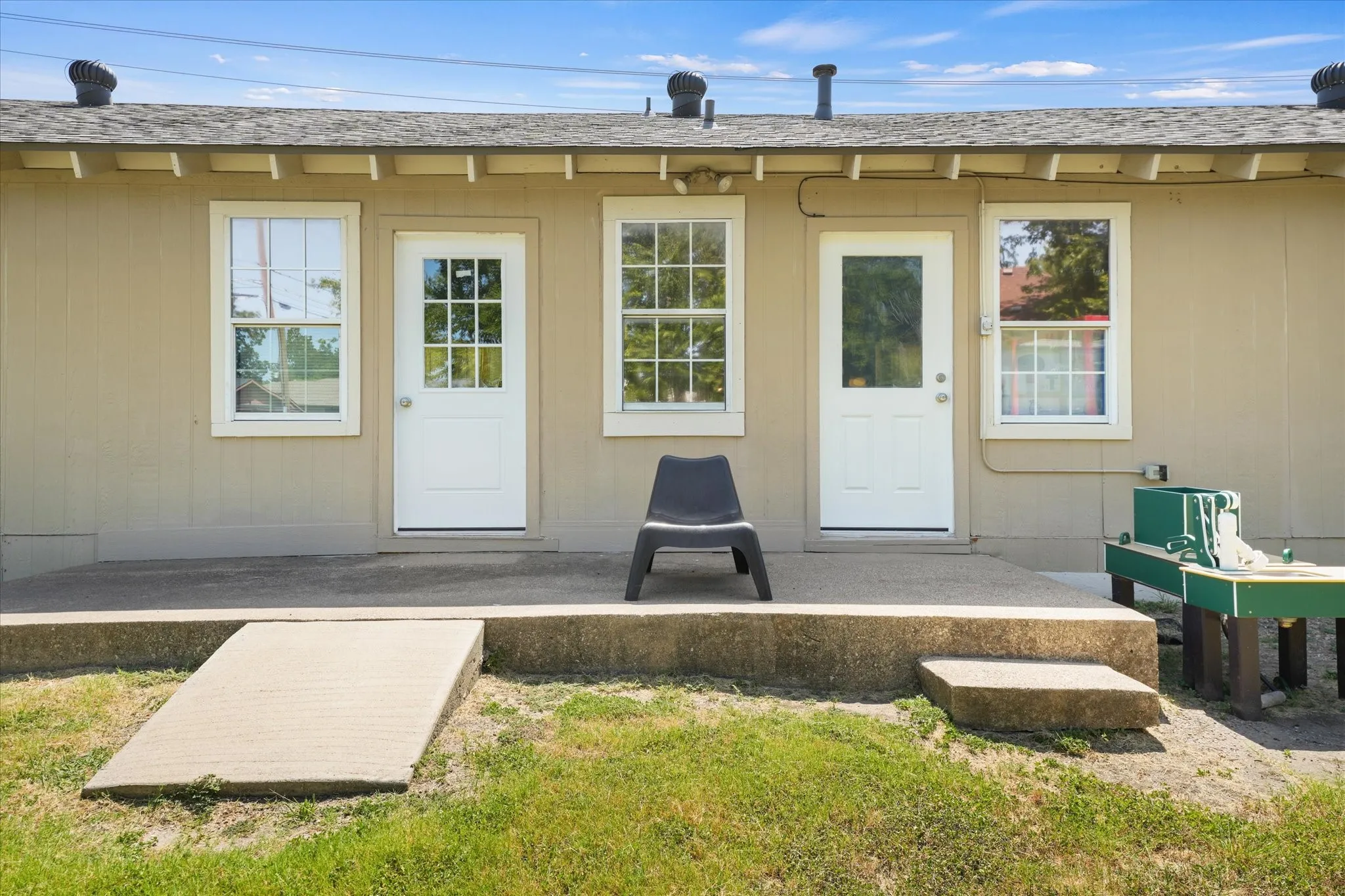 Rear exterior featuring a concrete patio, two doors with glass panels, two windows with white trim, and a concrete access ramp