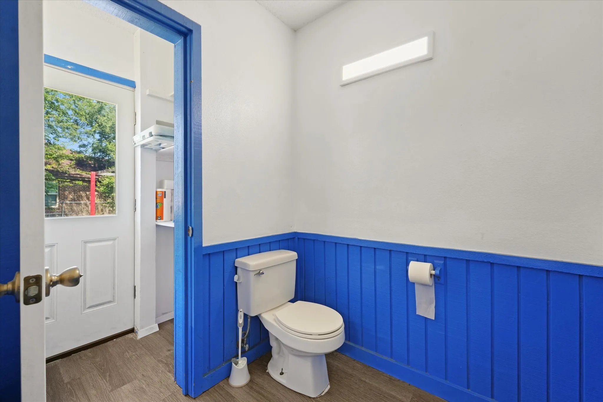 Bright half-bath featuring bold blue wainscoting, ceramic toilet with matching tank, wall-mounted paper holder, and recessed ceiling lighting