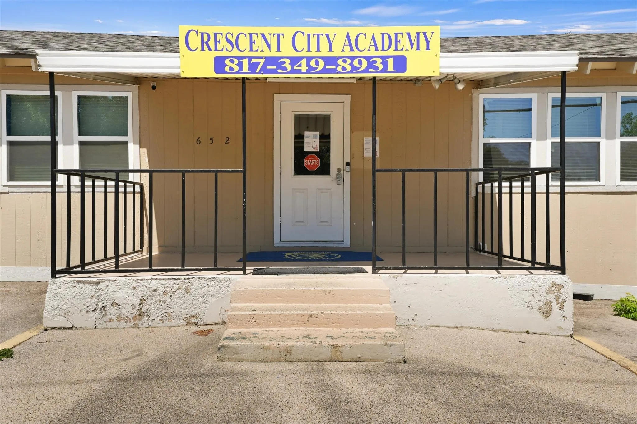 Welcoming front entrance featuring a centered glass and metal door, flanked by symmetrical black metal railings and multiple windows
