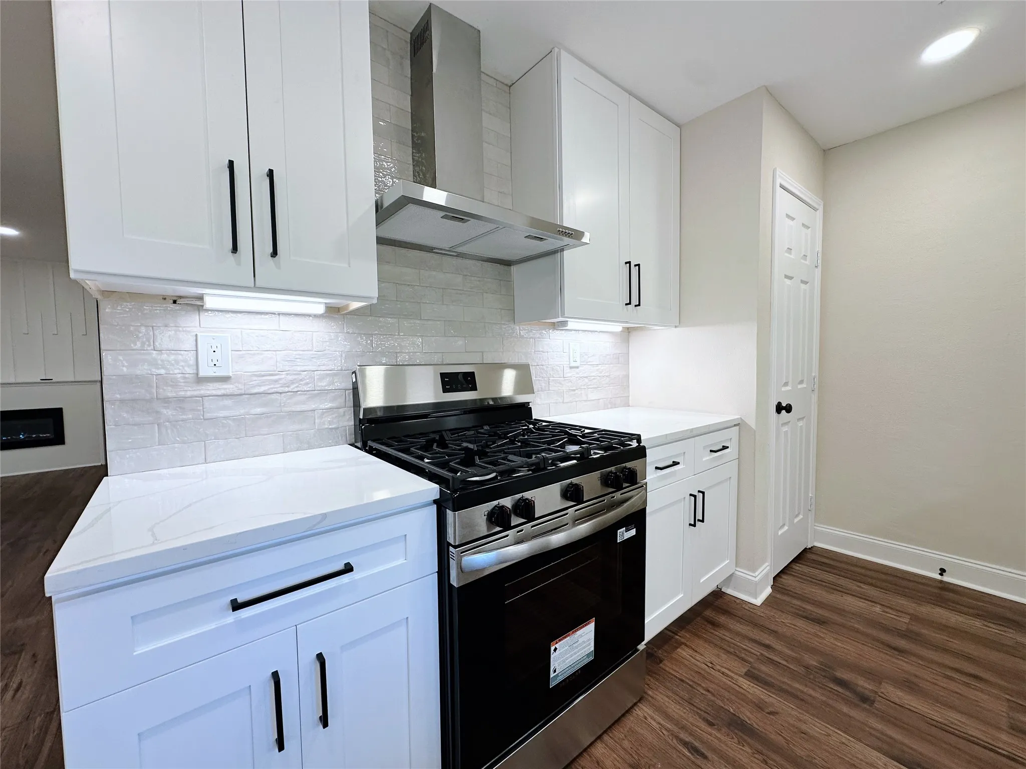 White shaker cabinetry with matte black hardware, stainless steel gas range, white quartz countertops, subway tile backsplash, and wood-finish flooring