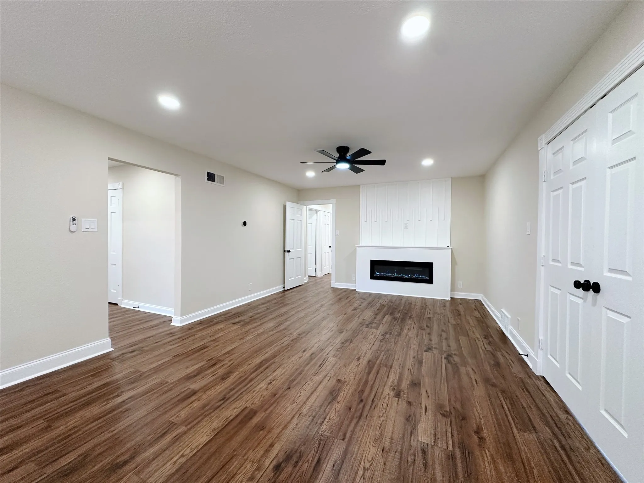 Wood-finish flooring throughout, featuring recessed ceiling lighting, a ceiling fan, and a fireplace with a white mantel and shiplap-style wall