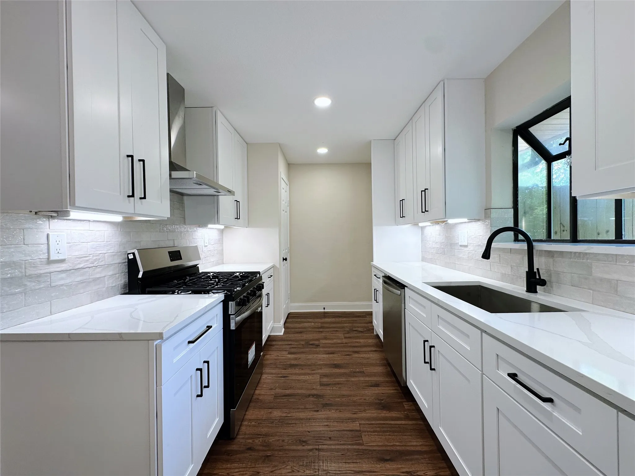 White shaker cabinetry with matte black hardware, stainless steel appliances, stone-look countertops, subway tile backsplash, and wood-finish flooring