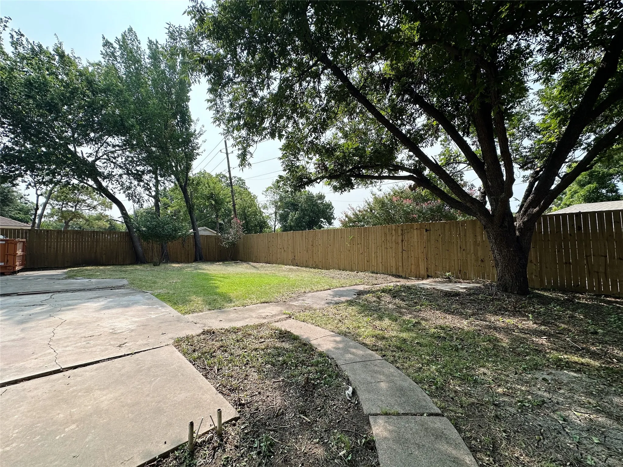 Expansive backyard featuring a new wood privacy fence, mature trees, concrete patio, and concrete pathway