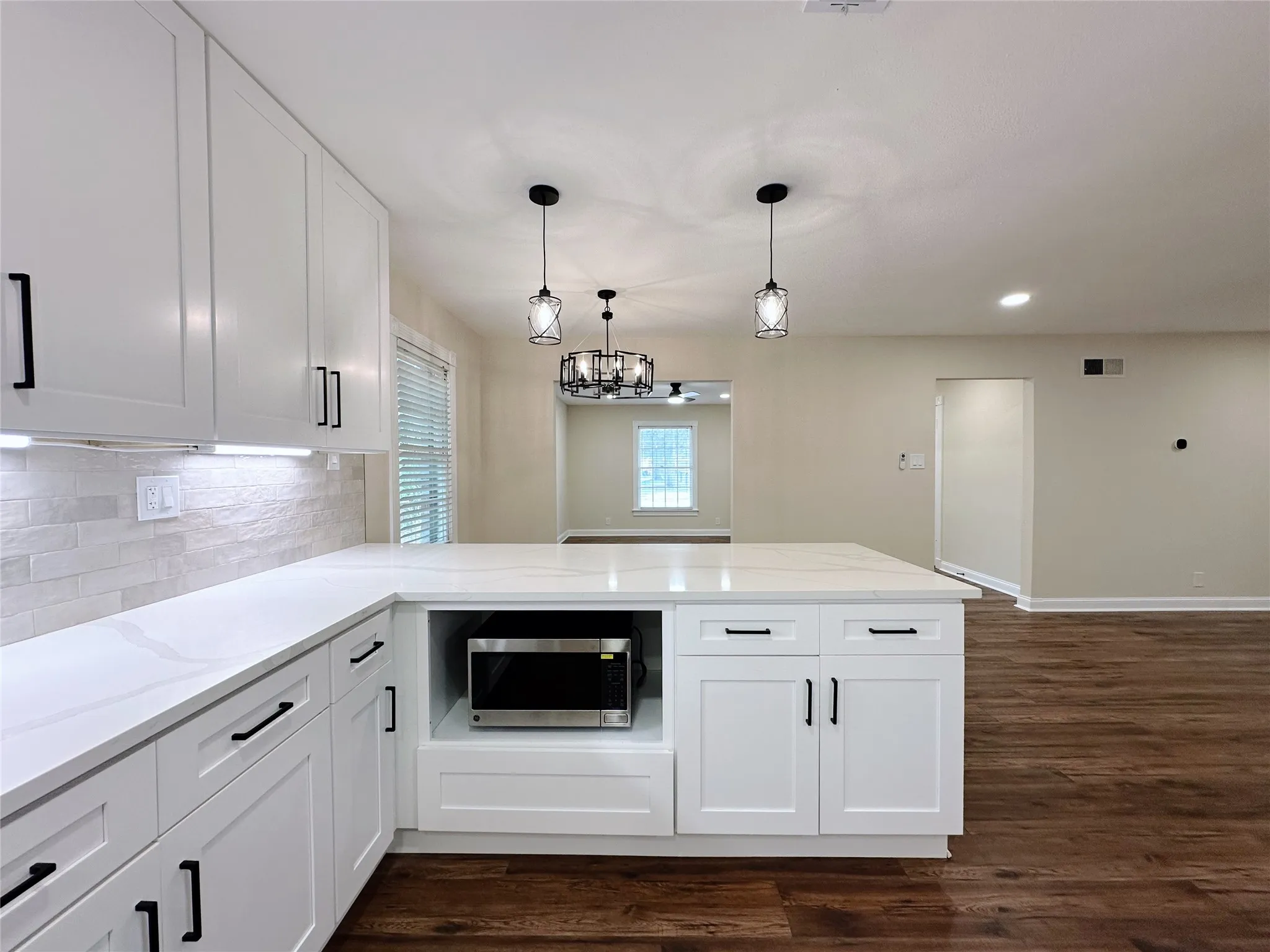 Contemporary kitchen featuring white shaker-style cabinetry with matte black hardware, white quartz countertops, subway tile backsplash, and a center island with integrated microwave