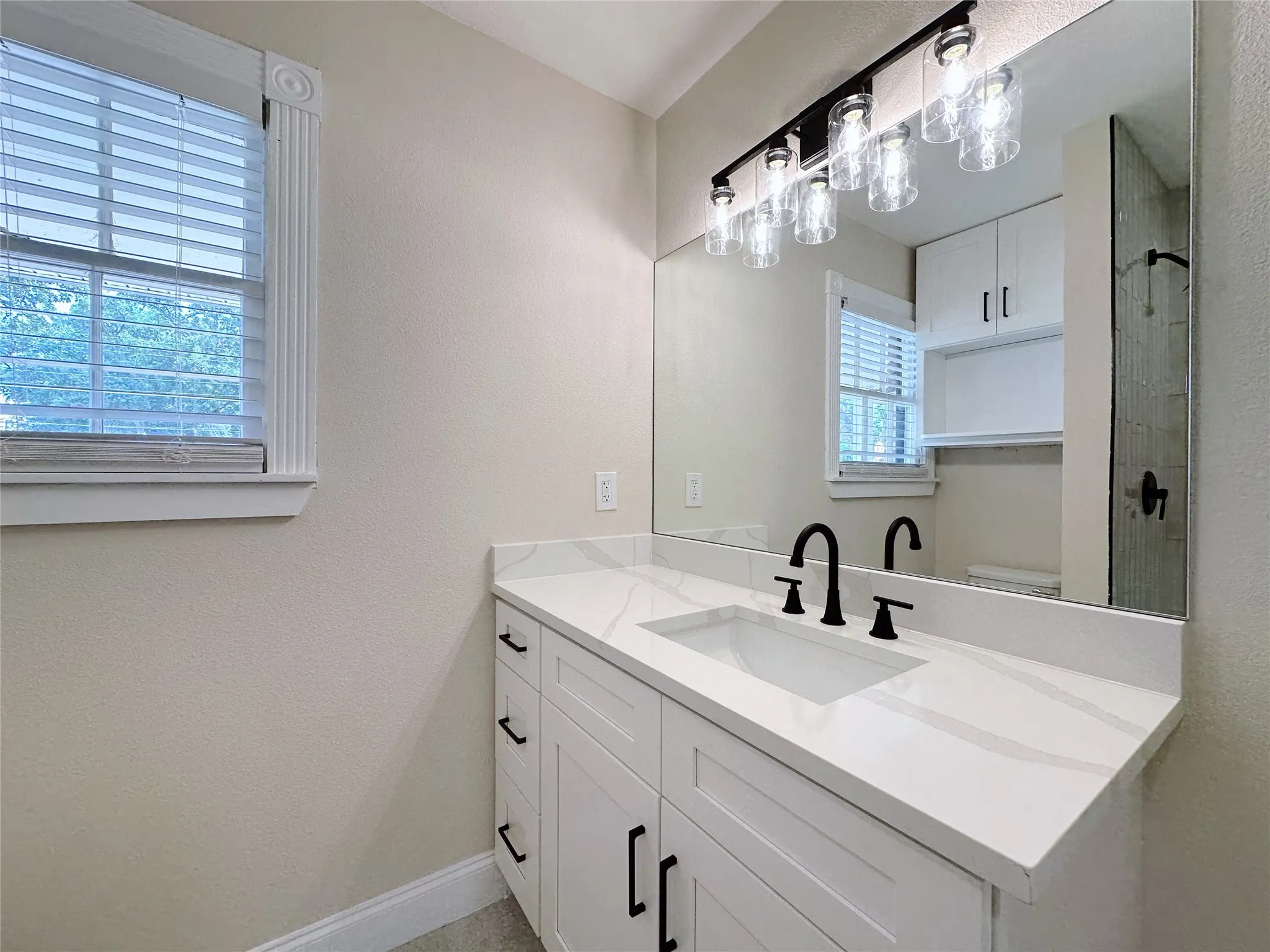 Modern vanity with a rectangular undermount sink, stone countertop, matte black faucet, and a large wall mirror