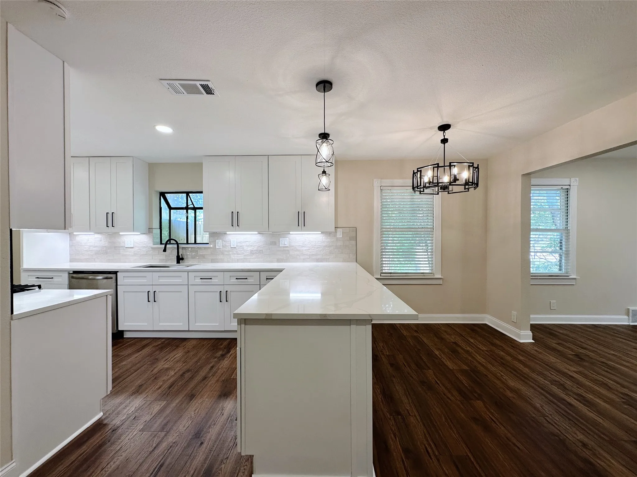 White cabinetry with dark hardware, stone-look countertops, subway tile backsplash, and dark wood-finish flooring