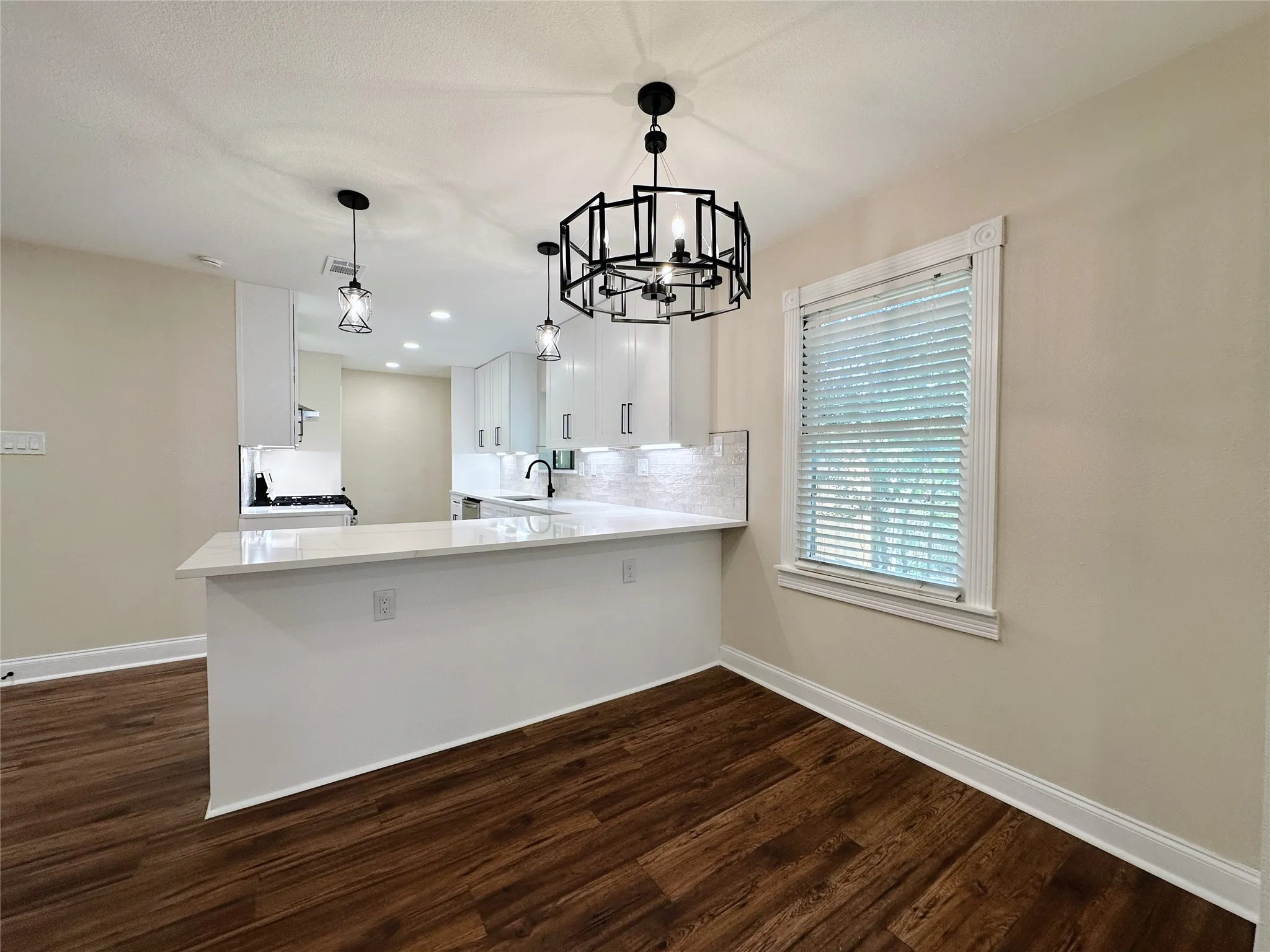 Wood-finish flooring, contemporary chandelier, recessed lighting, white cabinetry, and a kitchen peninsula with a light-toned countertop