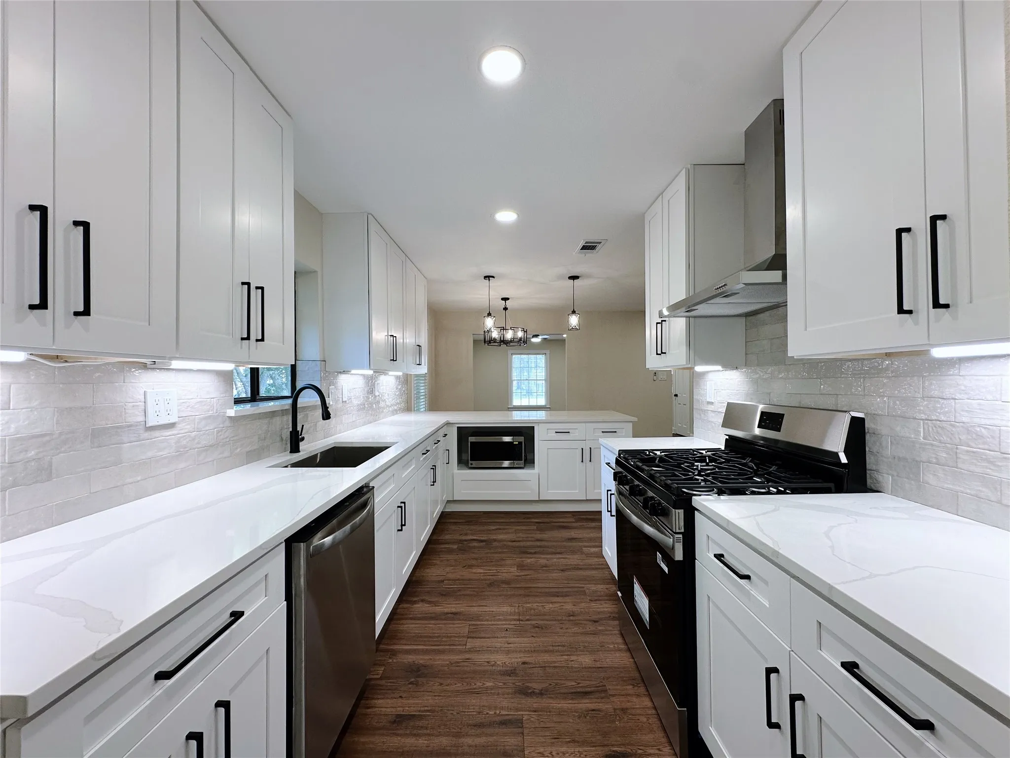 White shaker-style cabinetry with matte black hardware, white countertops, stainless steel appliances, wood-finish flooring, and subway tile backsplash