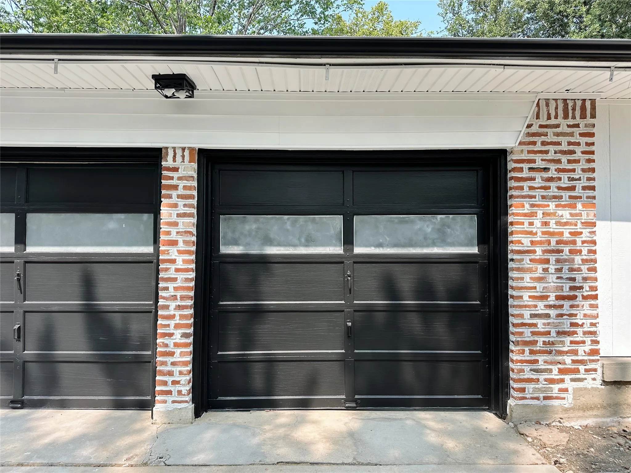 Dual garage doors with frosted window panels, brick pillar detailing, and an exterior light fixture