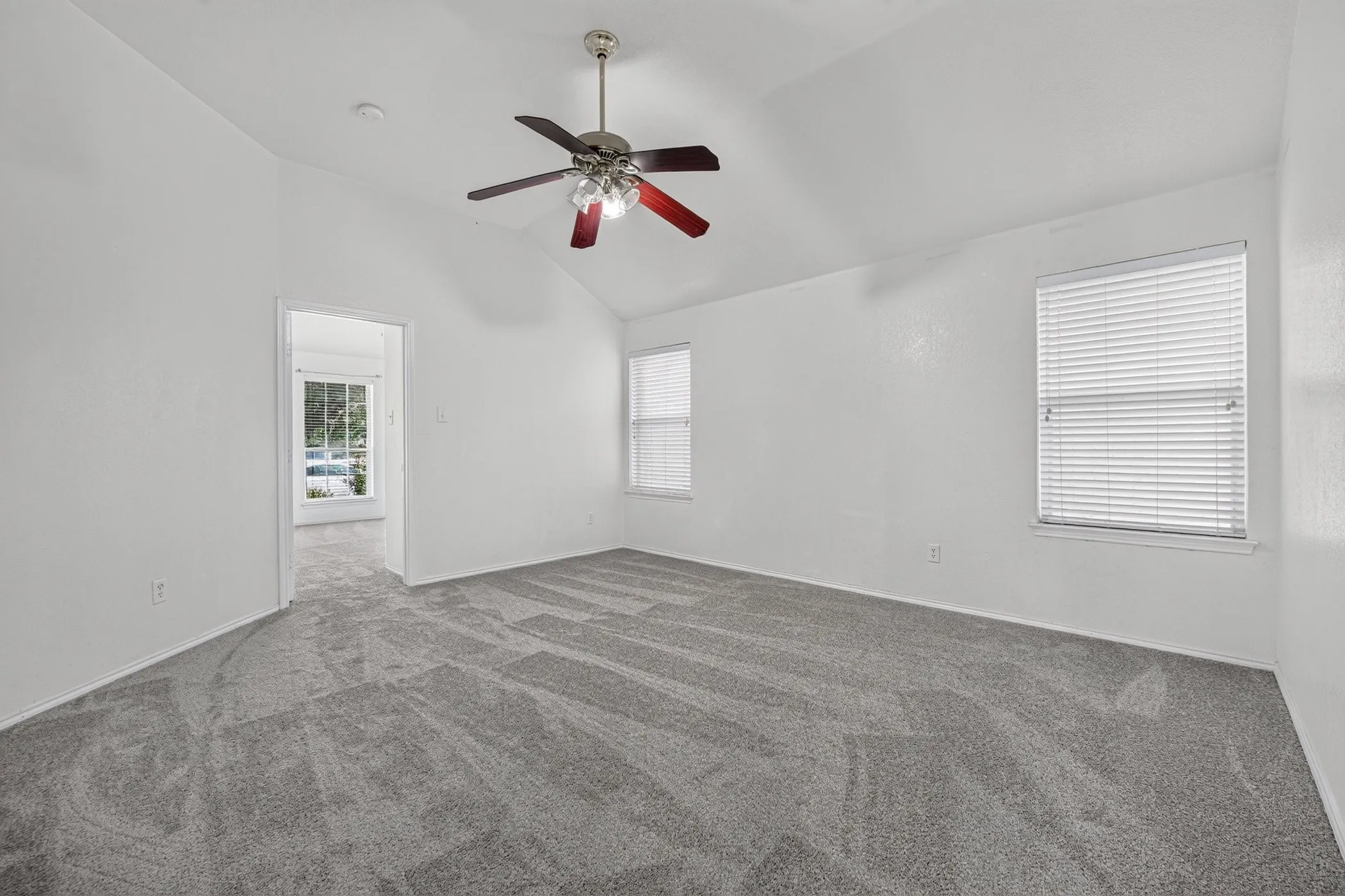 Spacious bedroom featuring neutral wall finishes, plush carpeting, a ceiling fan with integrated lighting, and abundant natural light from multiple windows with plantation shutters