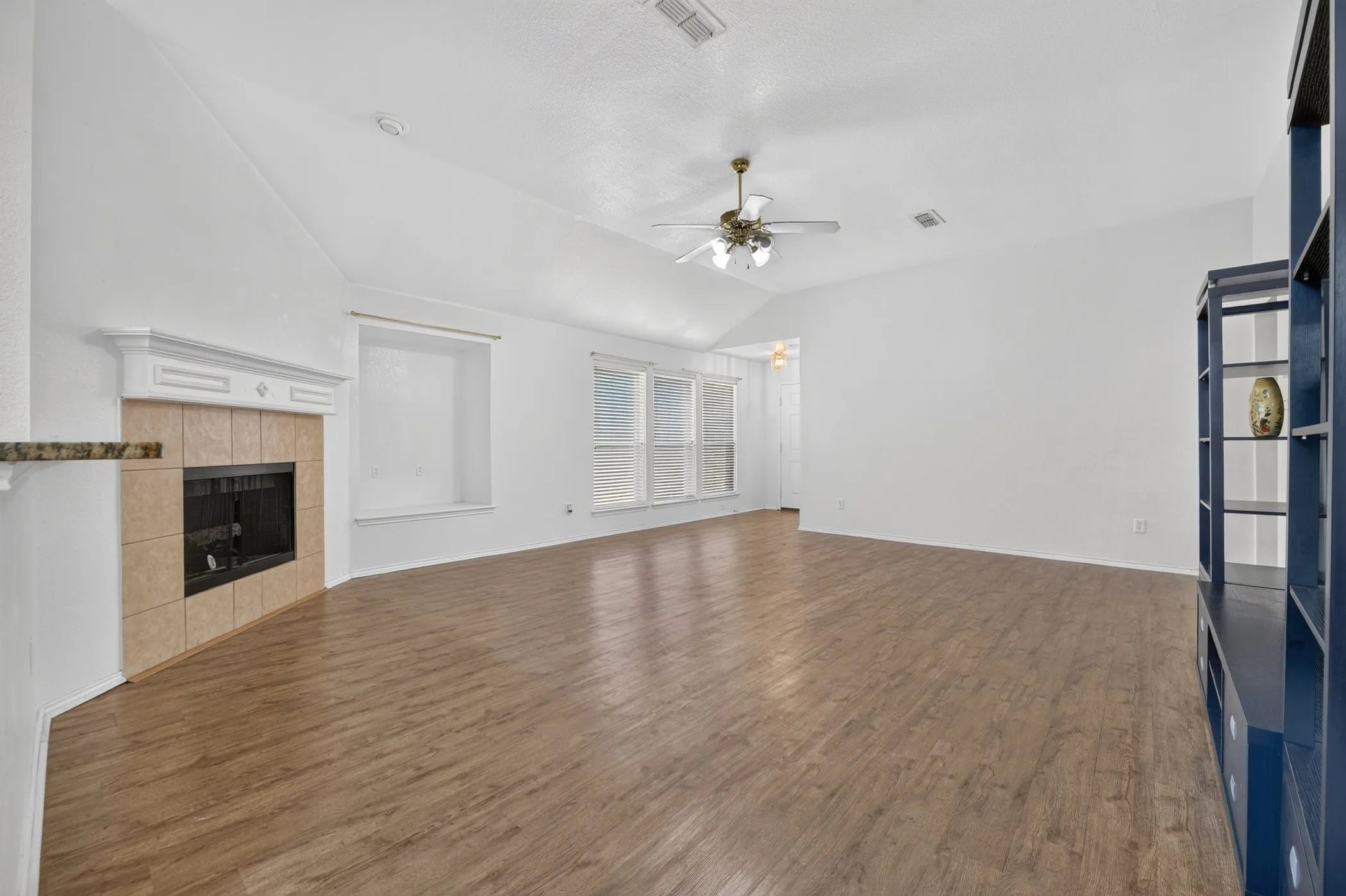 Spacious living area featuring high vaulted ceilings, wood-finish flooring, a tiled fireplace with a mantel, and built-in shelving
