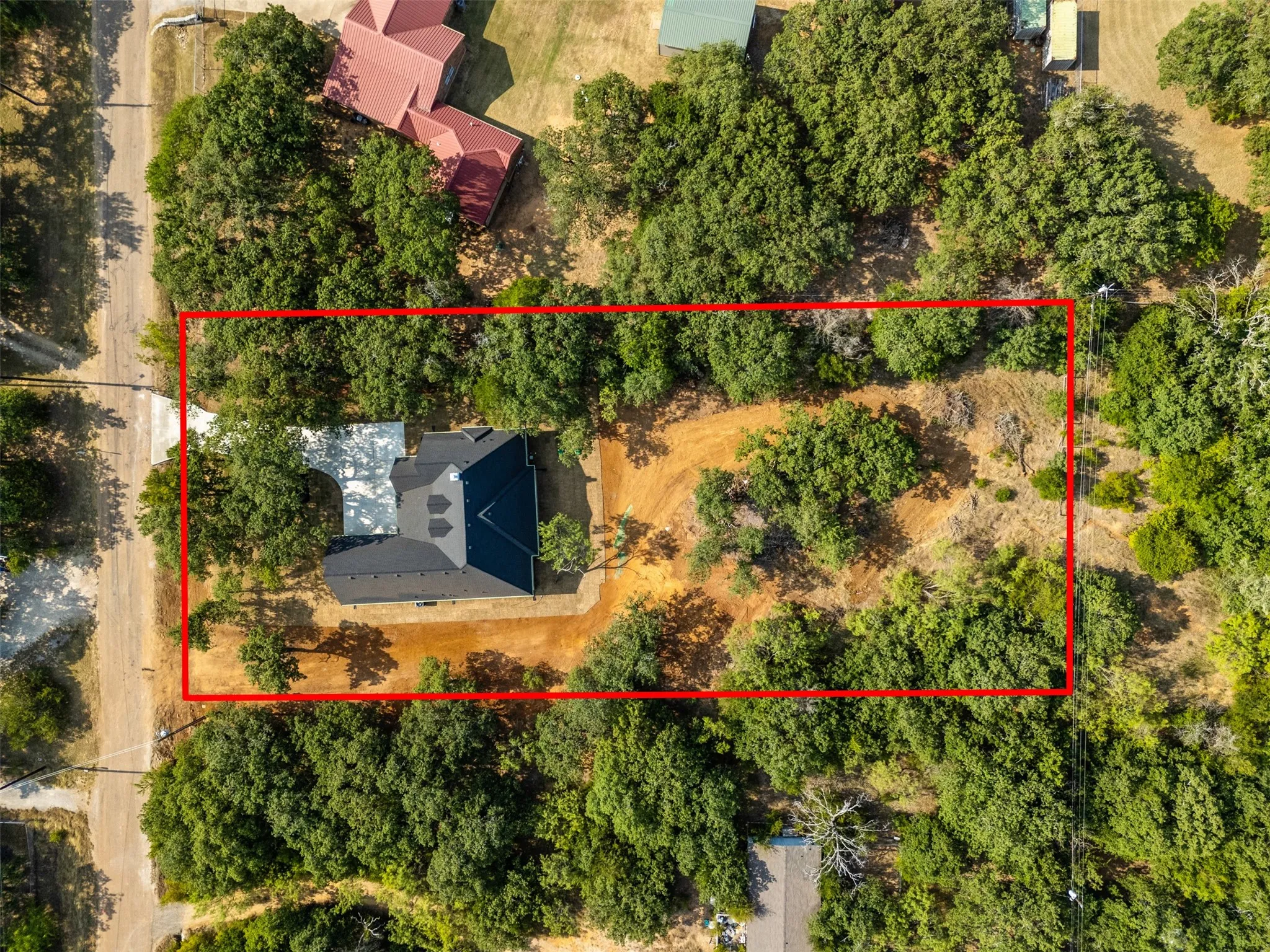 Expansive property featuring a dark-tiled roof, abundant mature trees, and a substantial unpaved driveway