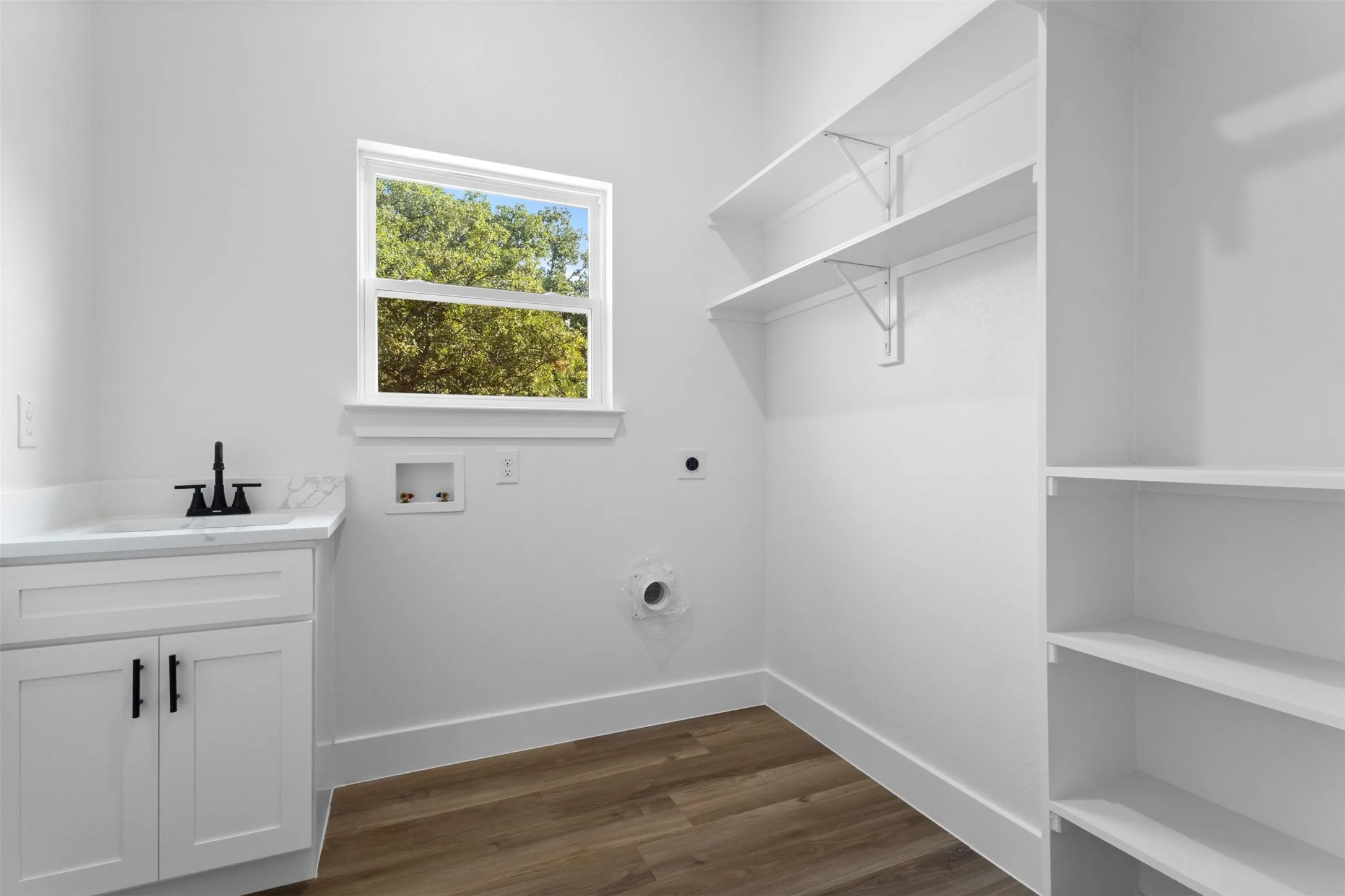 White cabinetry with black hardware, white countertop, wood-finish flooring, built-in shelving, and a window