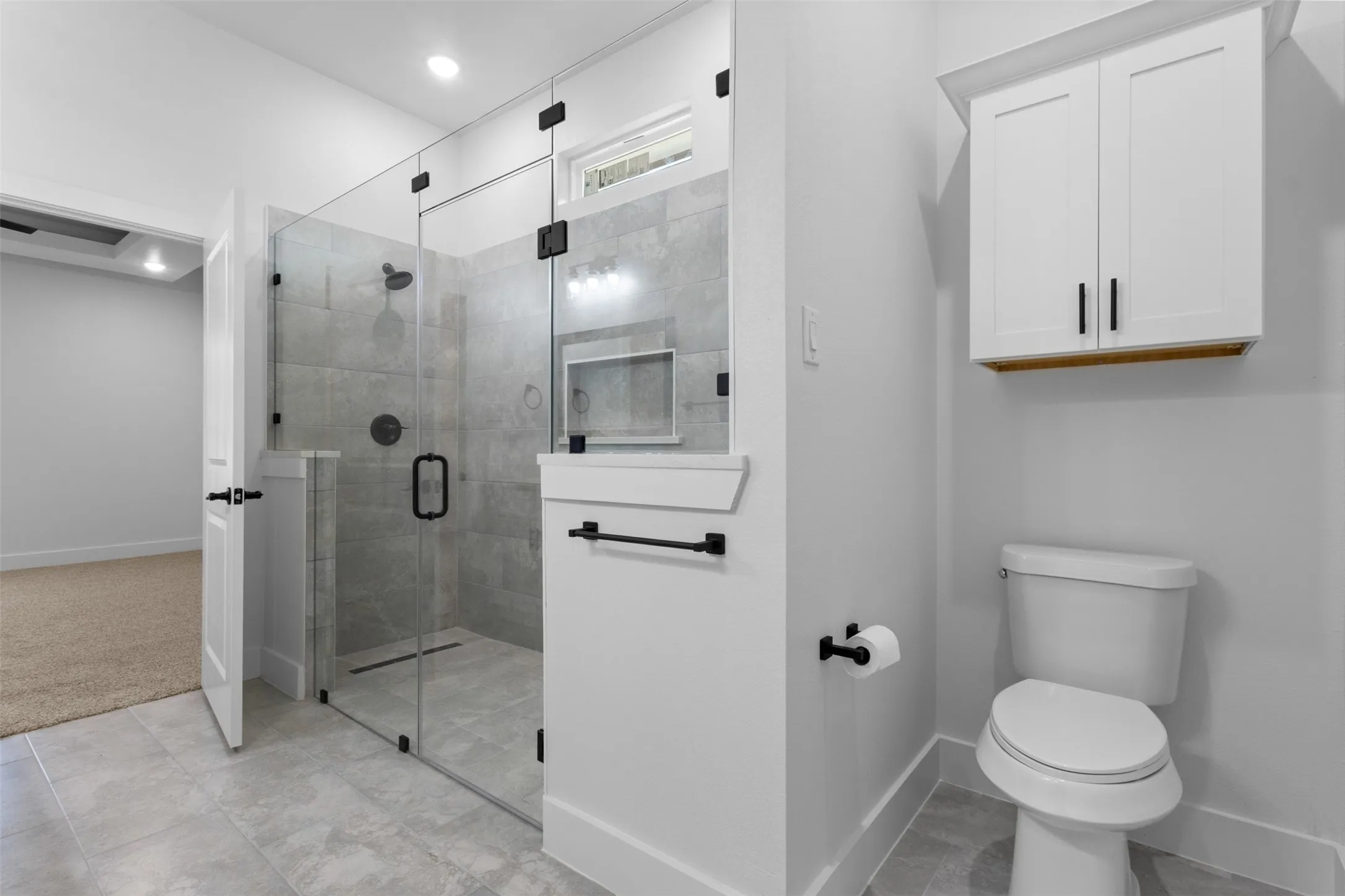 Glass-enclosed shower with a tiled surround and built-in niche, white wall-mounted cabinetry, and a white toilet