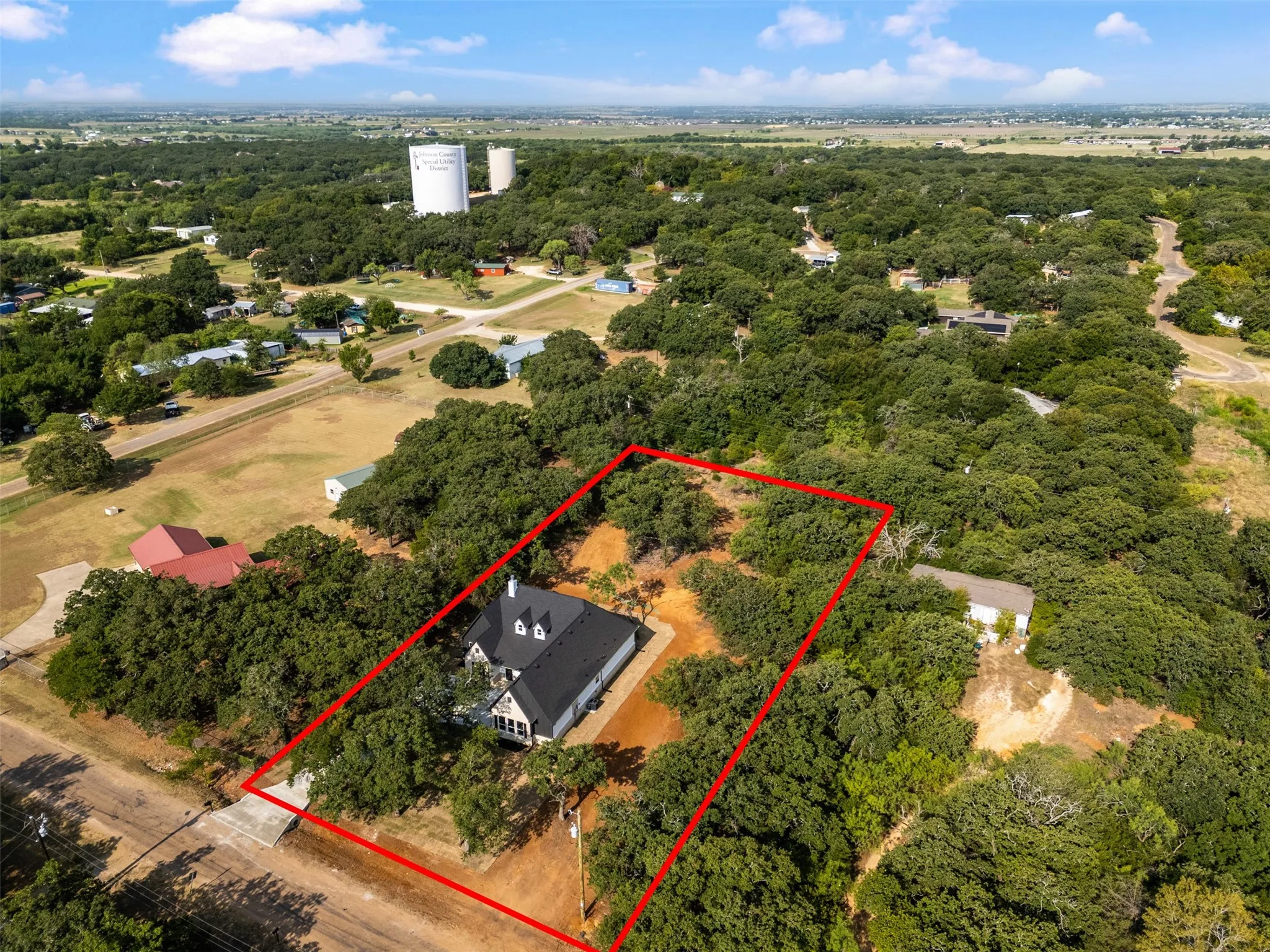 Aerial view of this rural property featuring a modern residence with a dark roof situated on expansive grounds surrounded by mature oak and native trees