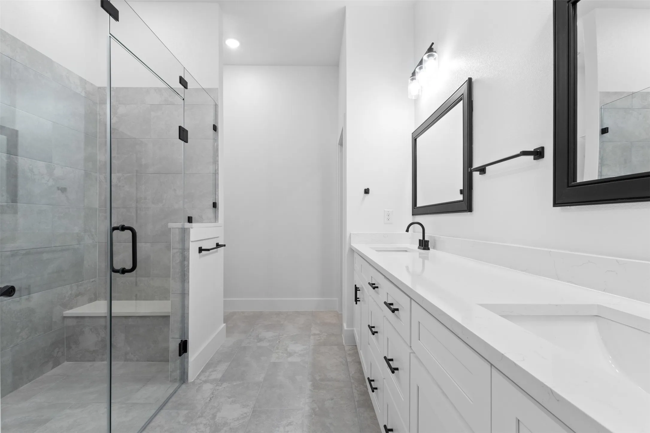 Glass-enclosed shower with a built-in bench, dual vanity with undermount sinks and white countertops, and matte black fixtures