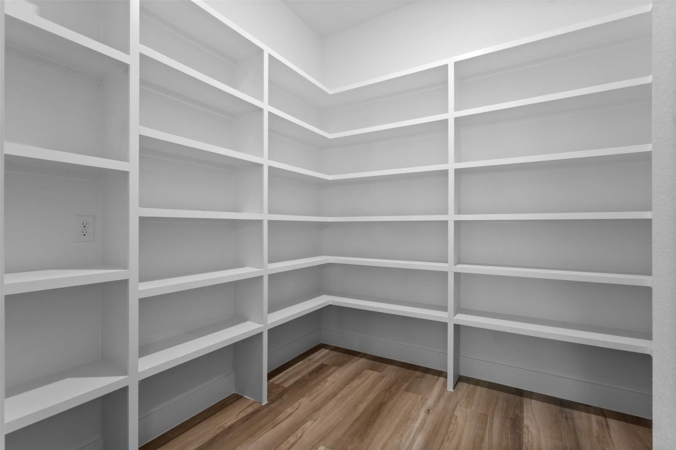 Built-in white shelving, expansive storage capacity, wood-finish flooring, and a wall outlet