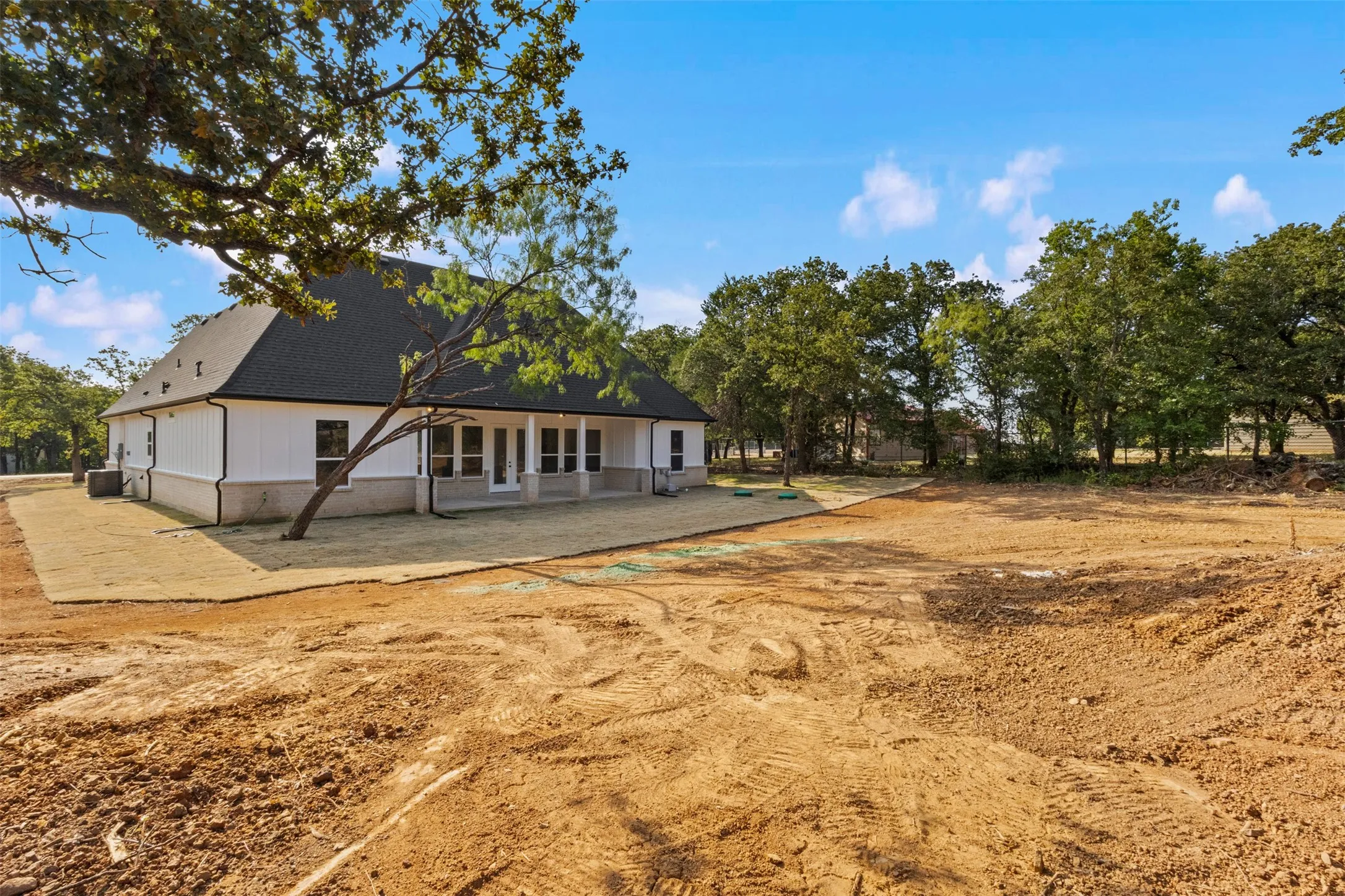 Charming residence with a black gable roof and white exterior, set on expansive grounds with mature shade trees