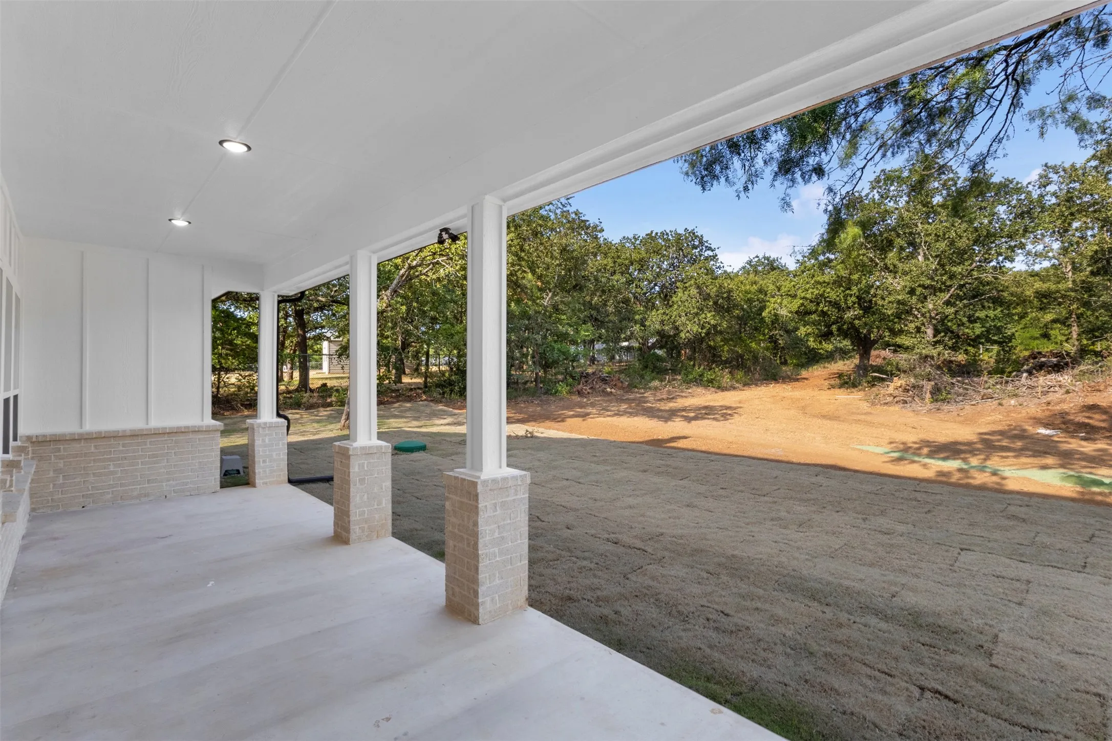 Expansive covered porch featuring recessed lighting, brick column bases, and a concrete surface
