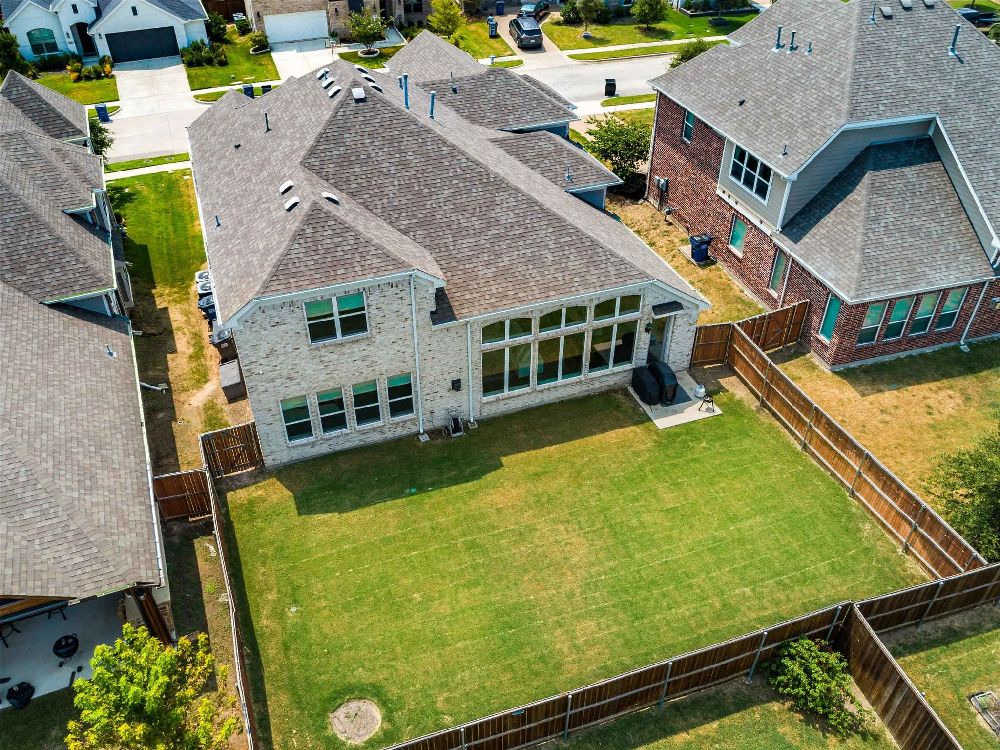 Expansive backyard with a manicured lawn, full perimeter fencing, and a brick exterior home featuring multiple windows