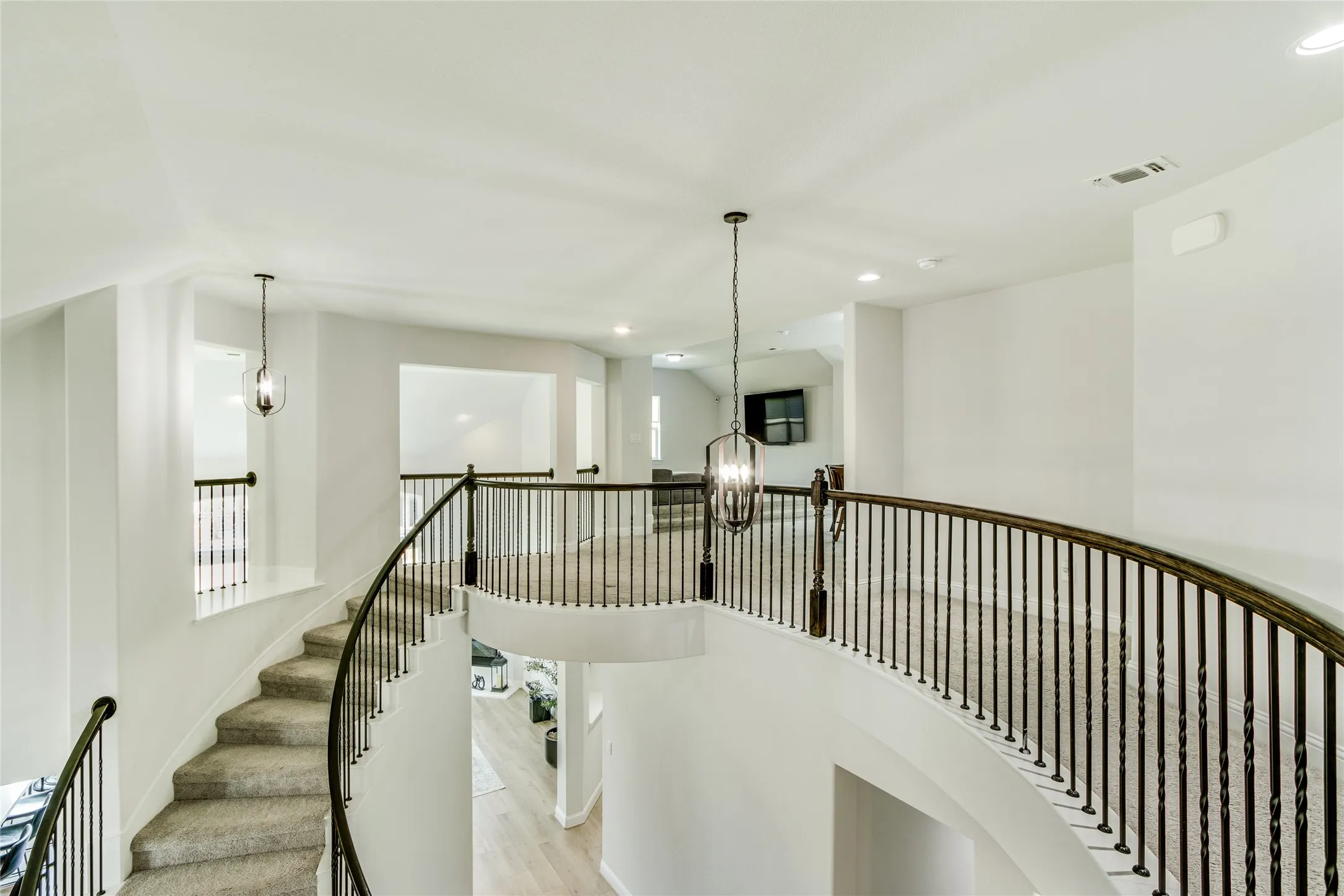Curved staircase with metal balusters and wood-finish handrail, recessed lighting, and suspended light fixtures