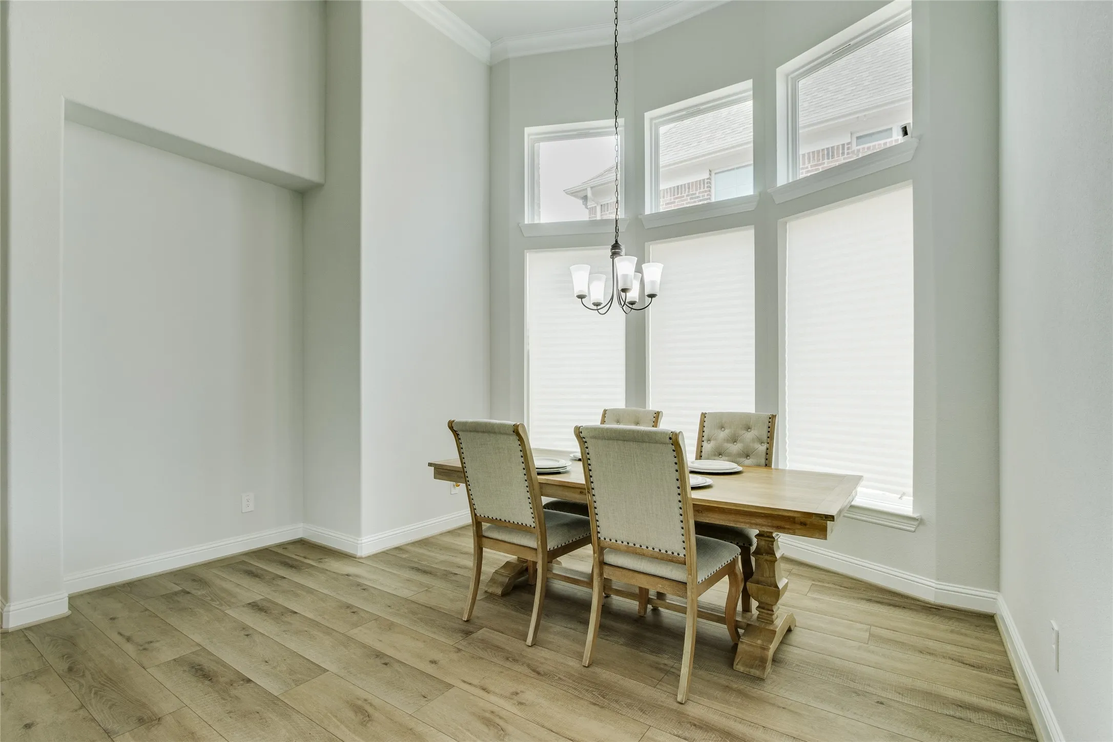 Wood-finish flooring, high ceilings, multiple windows with blinds, built-in chandelier, crown molding