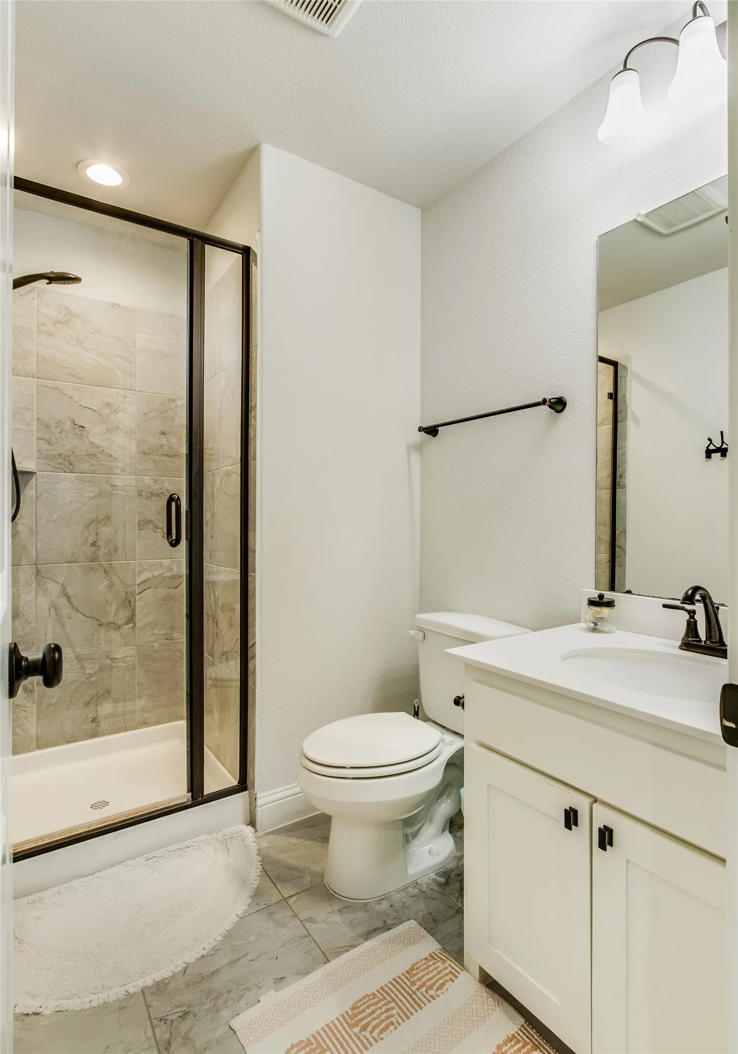 Contemporary bathroom featuring a walk-in shower with clear glass enclosure and tile surround, white vanity with integrated sink, dark bronze fixtures, and tile flooring