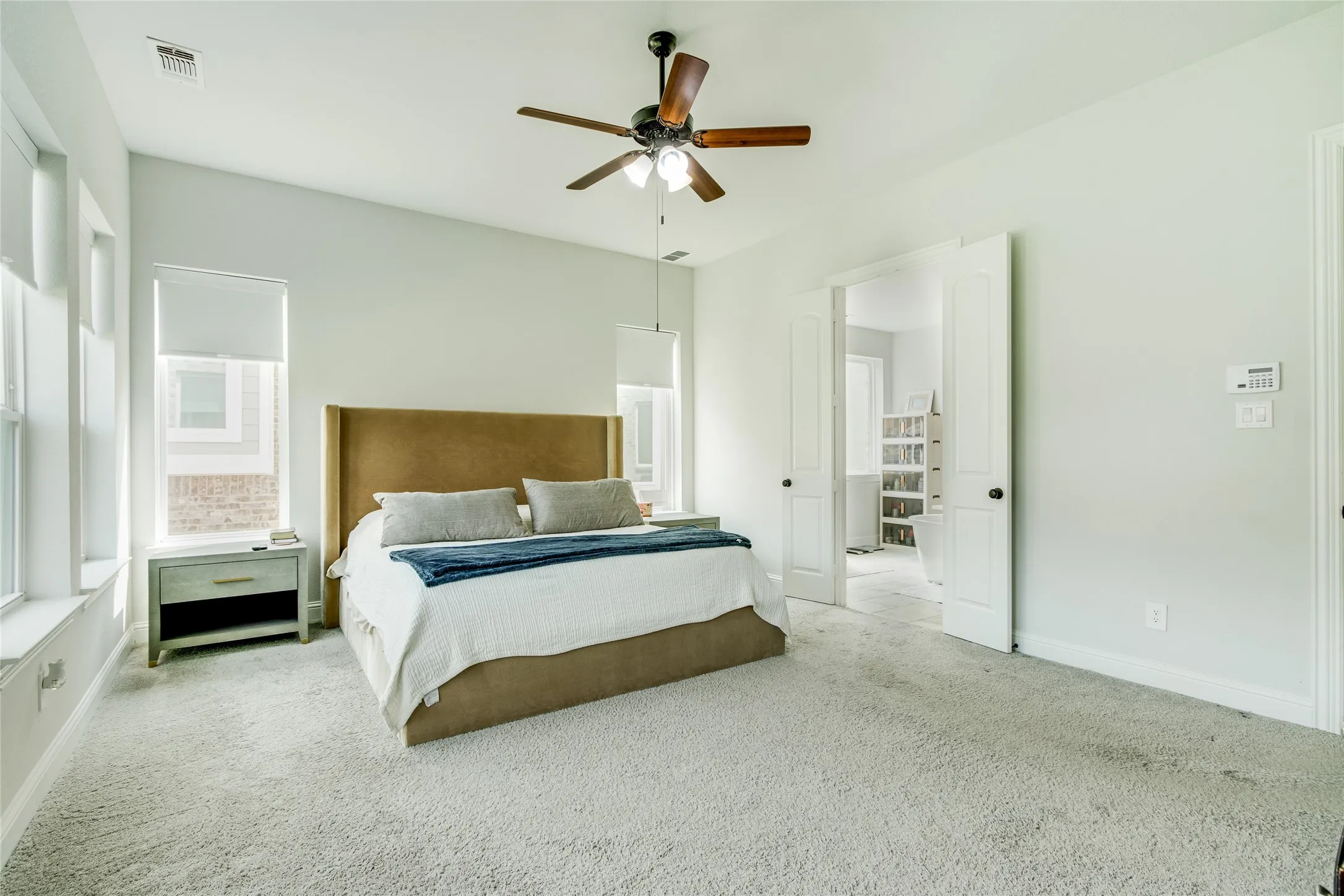 Vaulted ceiling with a wood-finish ceiling fan, multiple windows, carpet flooring, and double doors opening to an adjacent room
