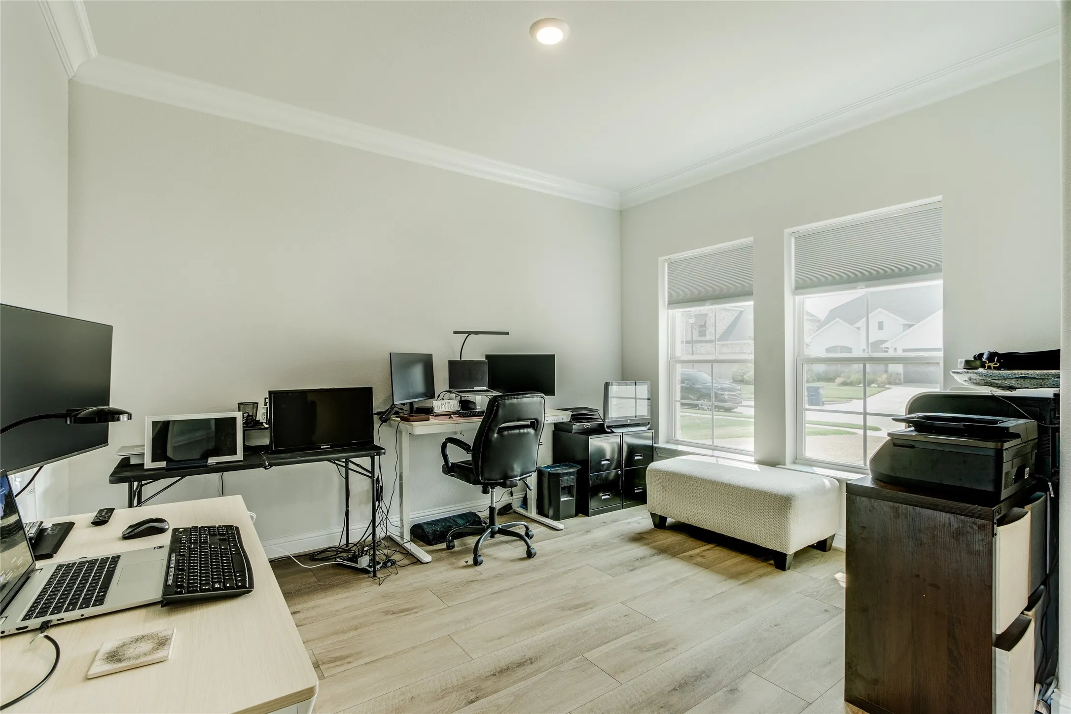 Spacious room with wood-finish flooring, crown molding, recessed lighting, and two large windows with roller shades
