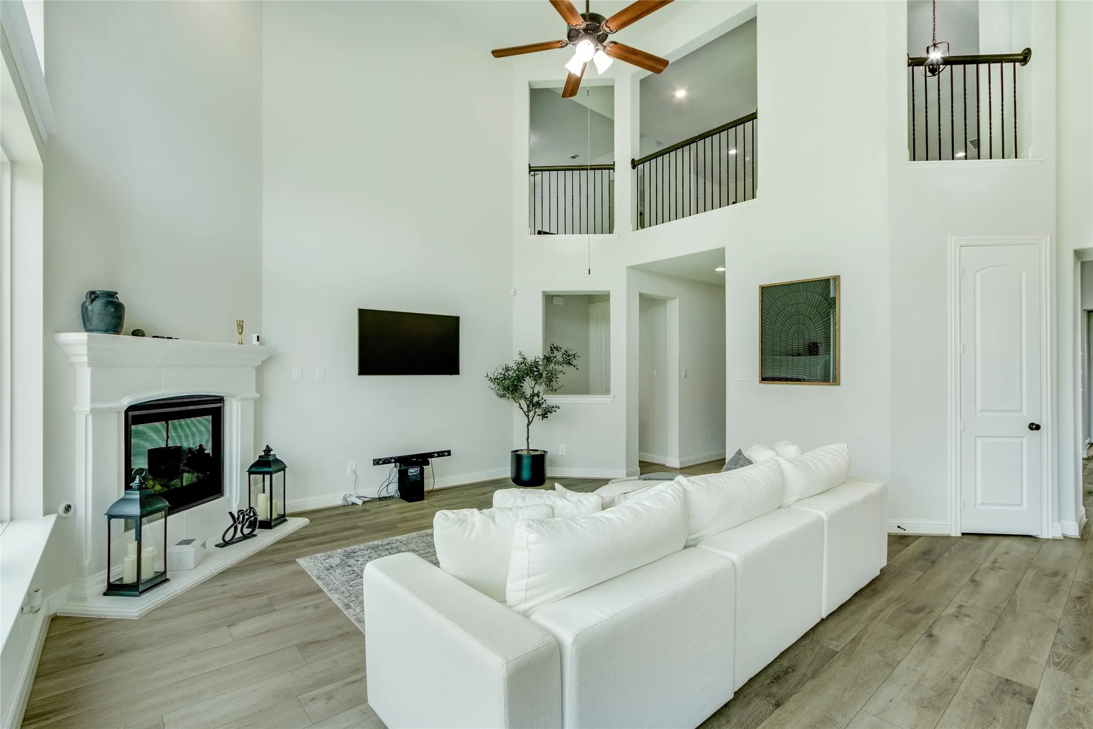 Soaring two-story great room with abundant natural light, ceiling fan, and gas fireplace with decorative surround
