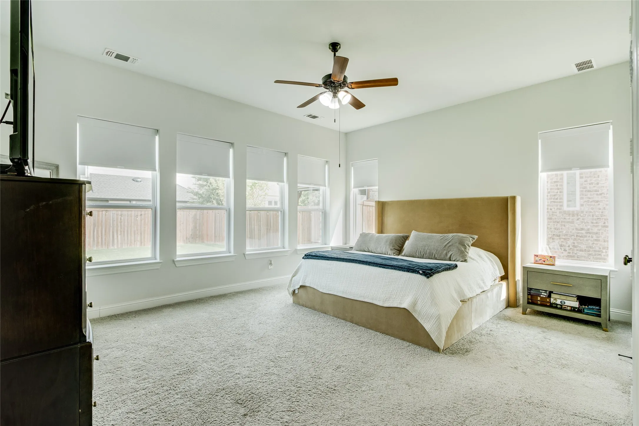 Bright interior with white walls, carpeted flooring, a ceiling fan with integrated lighting, and multiple windows with roller shades