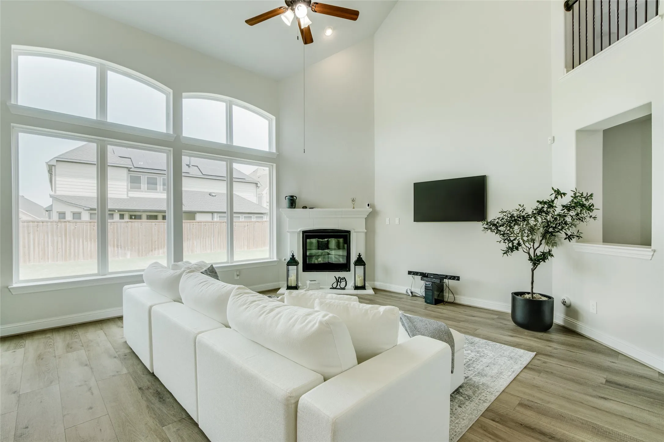 Two-story living area with high ceilings, large windows, wood-finish flooring, and a ceiling fan